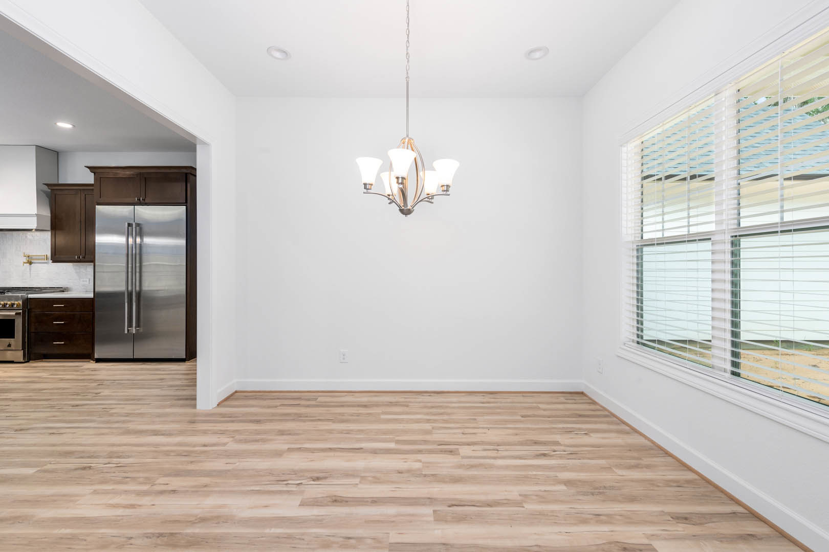 Open kitchen and dining area with hardwood floors, stainless steel refrigerator, modern chandelier, white walls, window blinds, and built-in microwave.