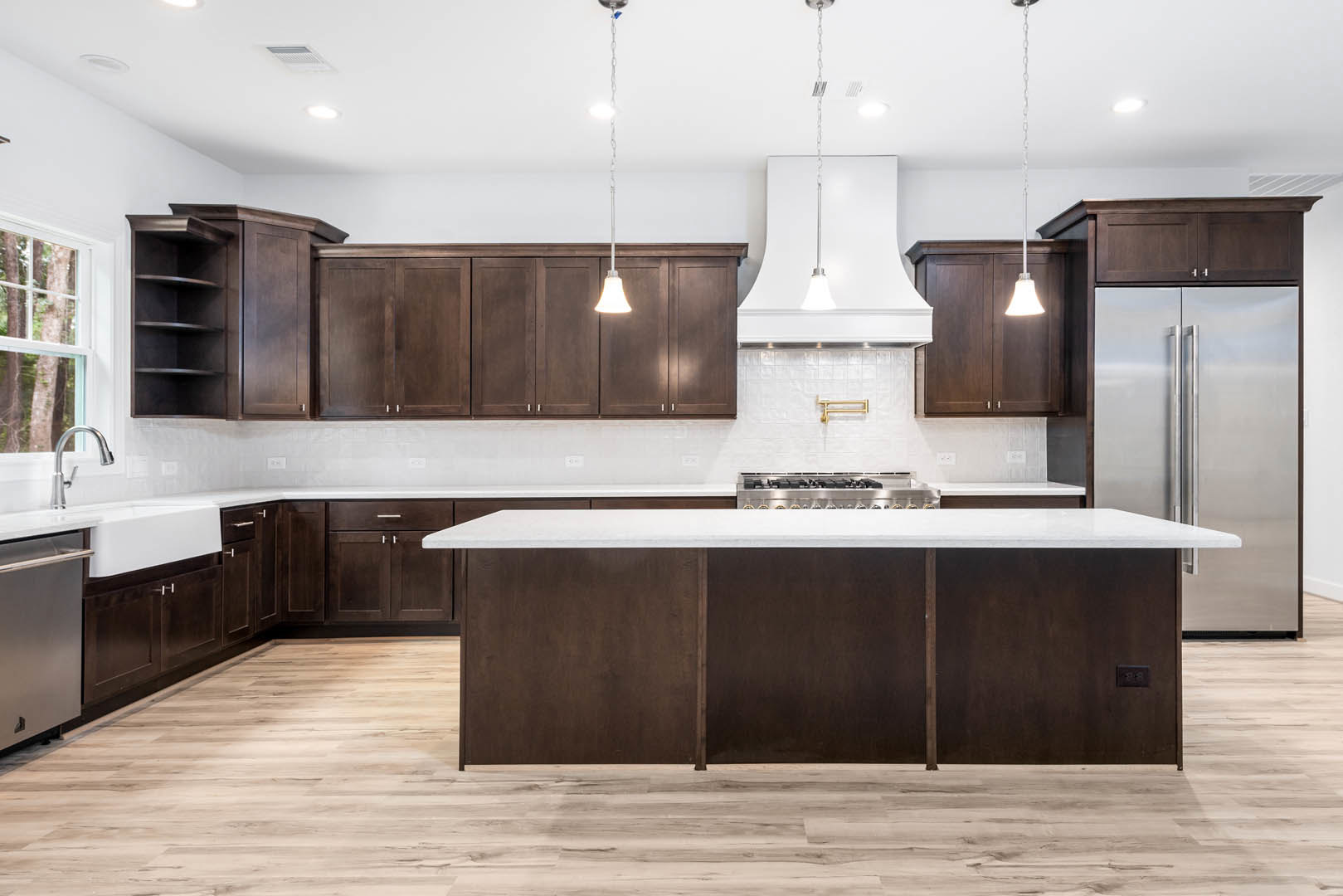 Dark wood kitchen cabinets, white quartz countertops, stainless steel stove and refrigerator, pendant light fixture, tile backsplash, hardwood flooring