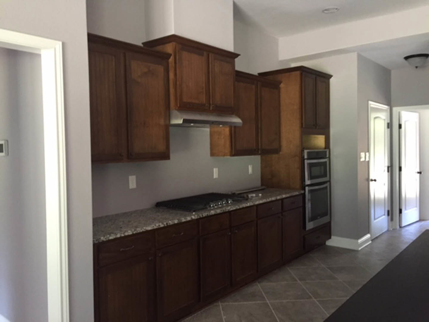Kitchen with natural wood cabinets, granite countertops, stainless steel refrigerator, dark brown tile flooring, and a white door illuminated by sunlight.