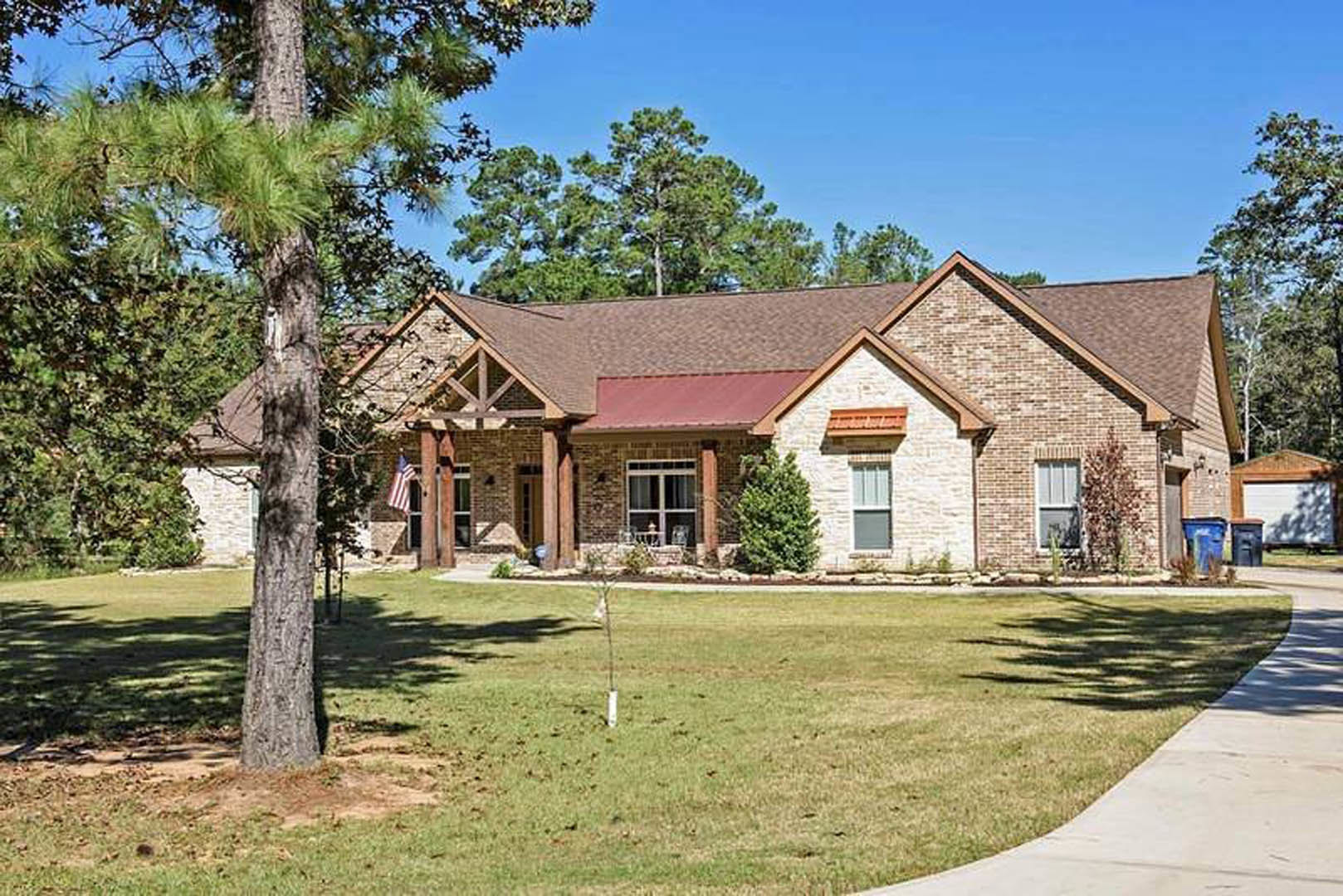 Two-story house with red roof, white-framed windows, covered porch, green lawn, and leafy trees in front