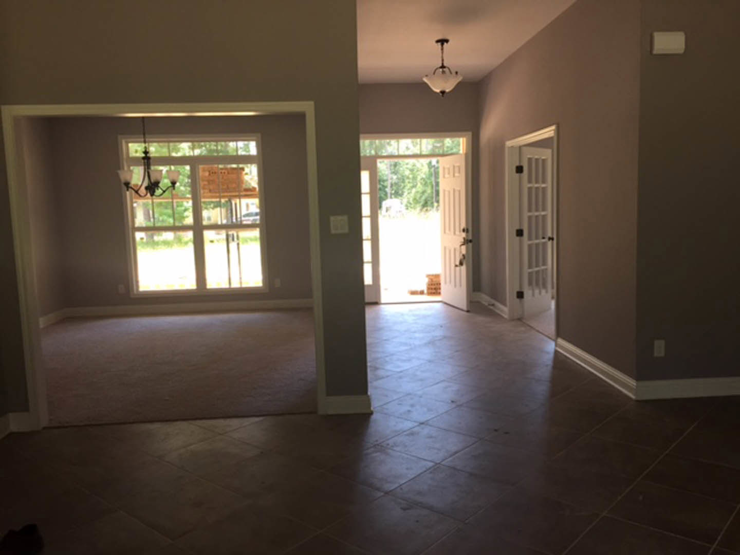 Open white door with black trim leading to adjacent room, laminate flooring, white walls, ceiling chandelier, window partially visible