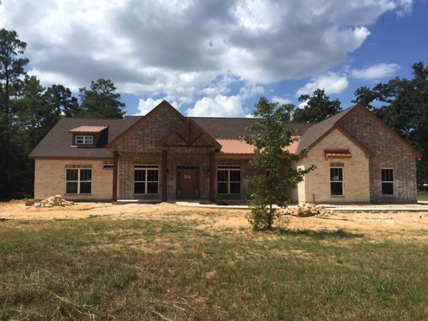 Two-story home with white siding, large windows, front door, manicured lawn, mature trees, and partly cloudy sky