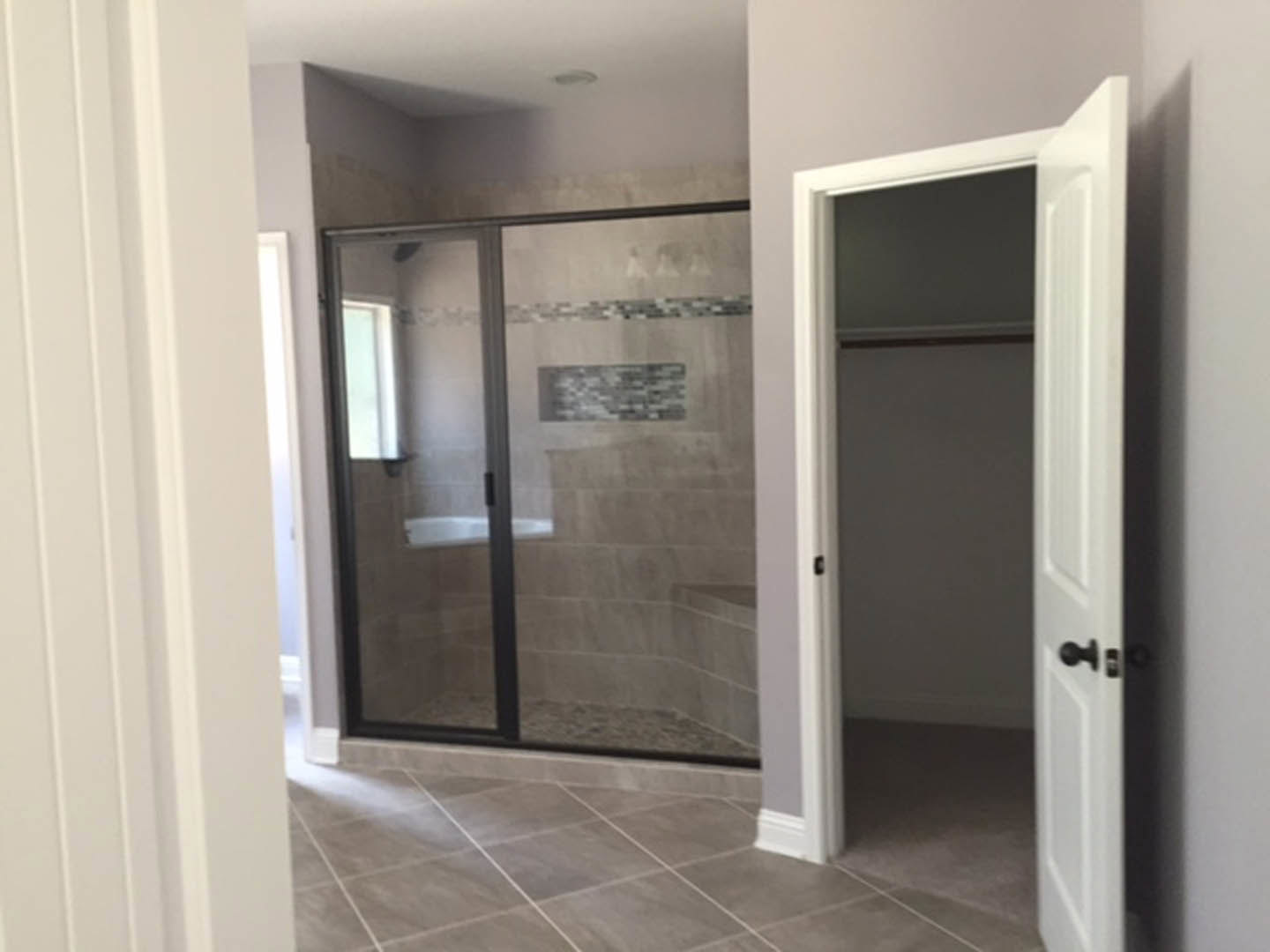 Bathroom featuring a walk-in shower with glass enclosure, tiled floor, open door leading to adjacent room, and modern fixtures