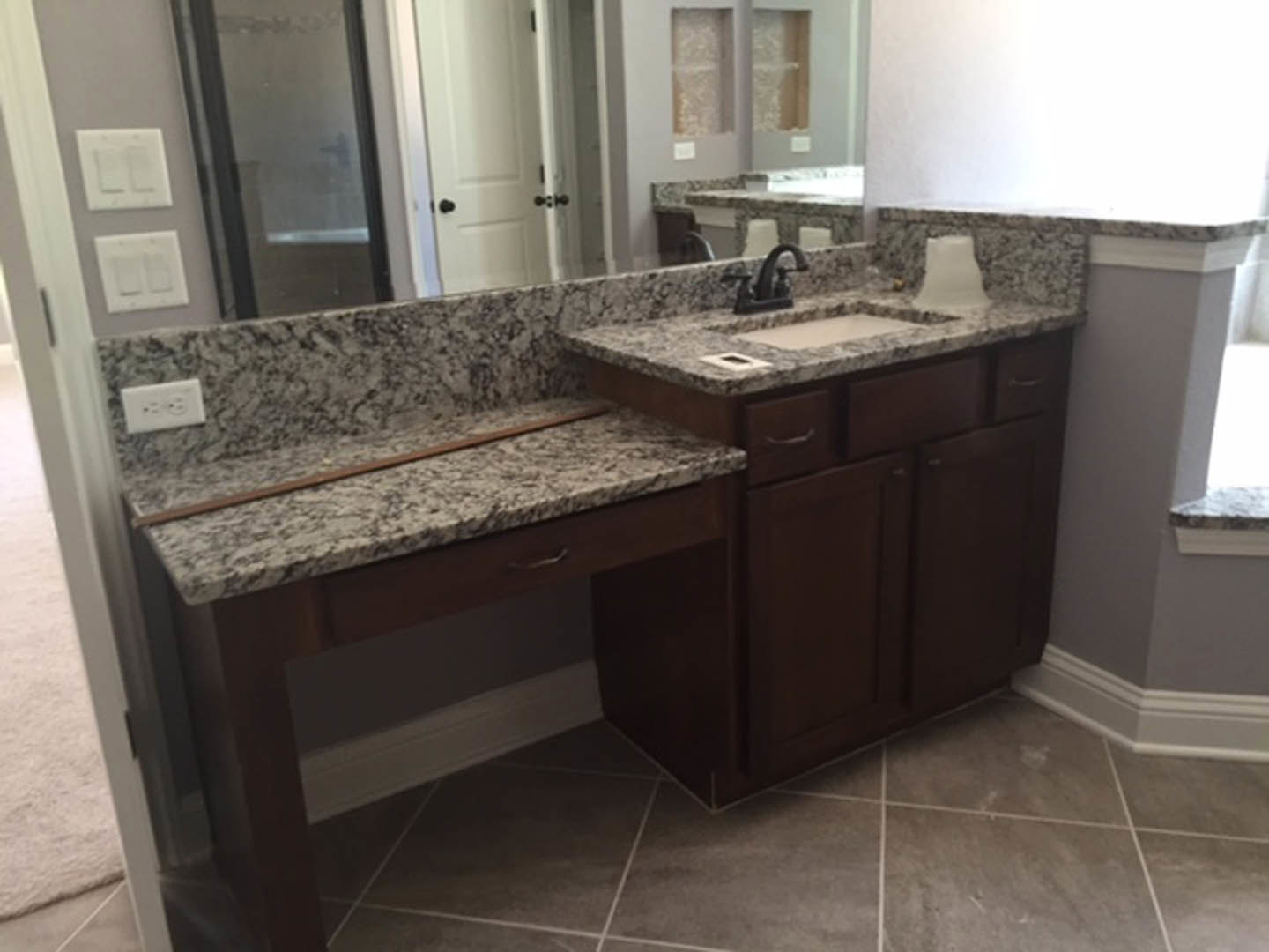 Marble bathroom countertop with undermount sink, chrome faucet, white tile floor, glass shower door with black frame, white wall featuring light switch and electrical outlet