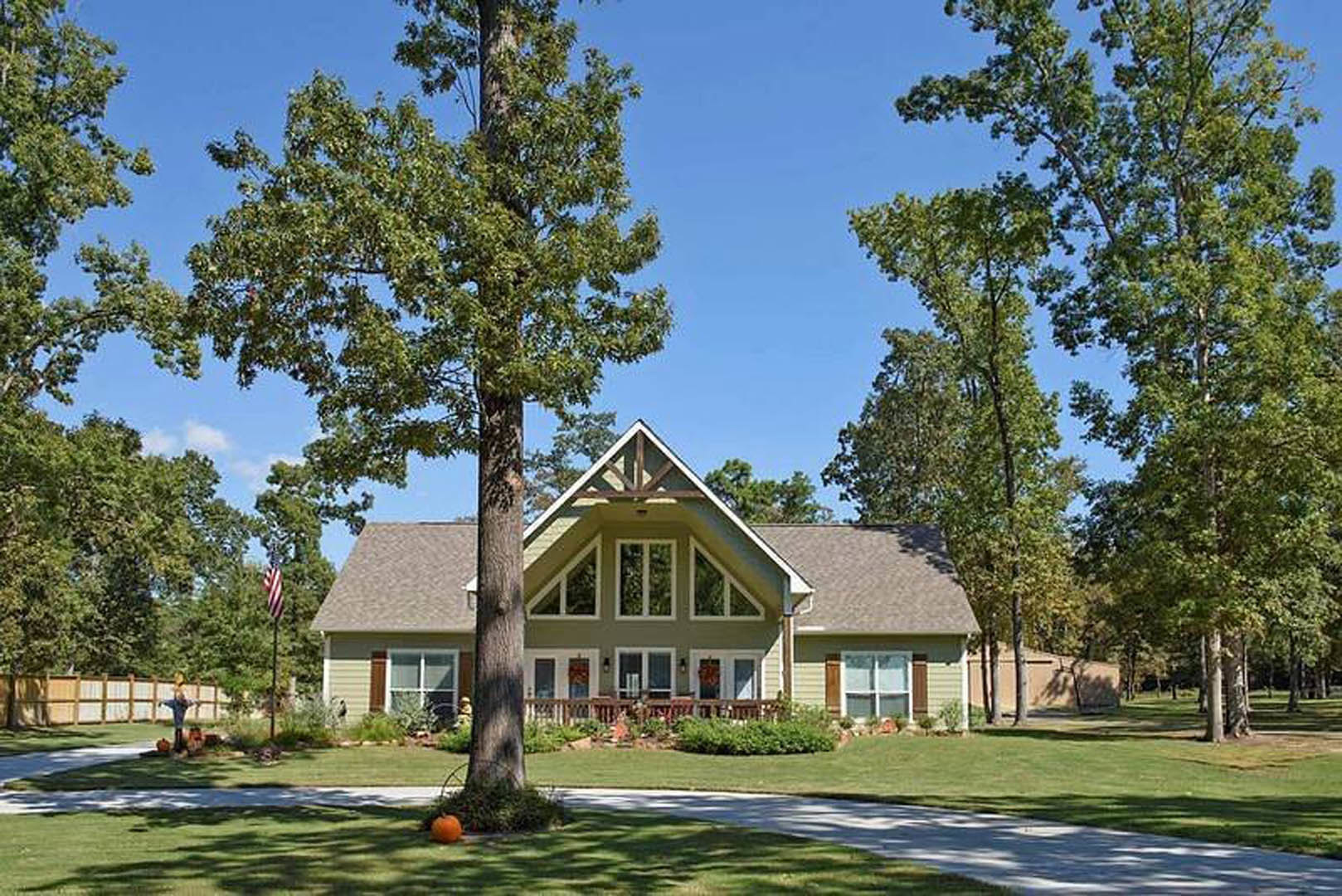 Two-story house with light siding, expansive green lawn, mature trees, stone walkway, and landscaped yard under blue sky