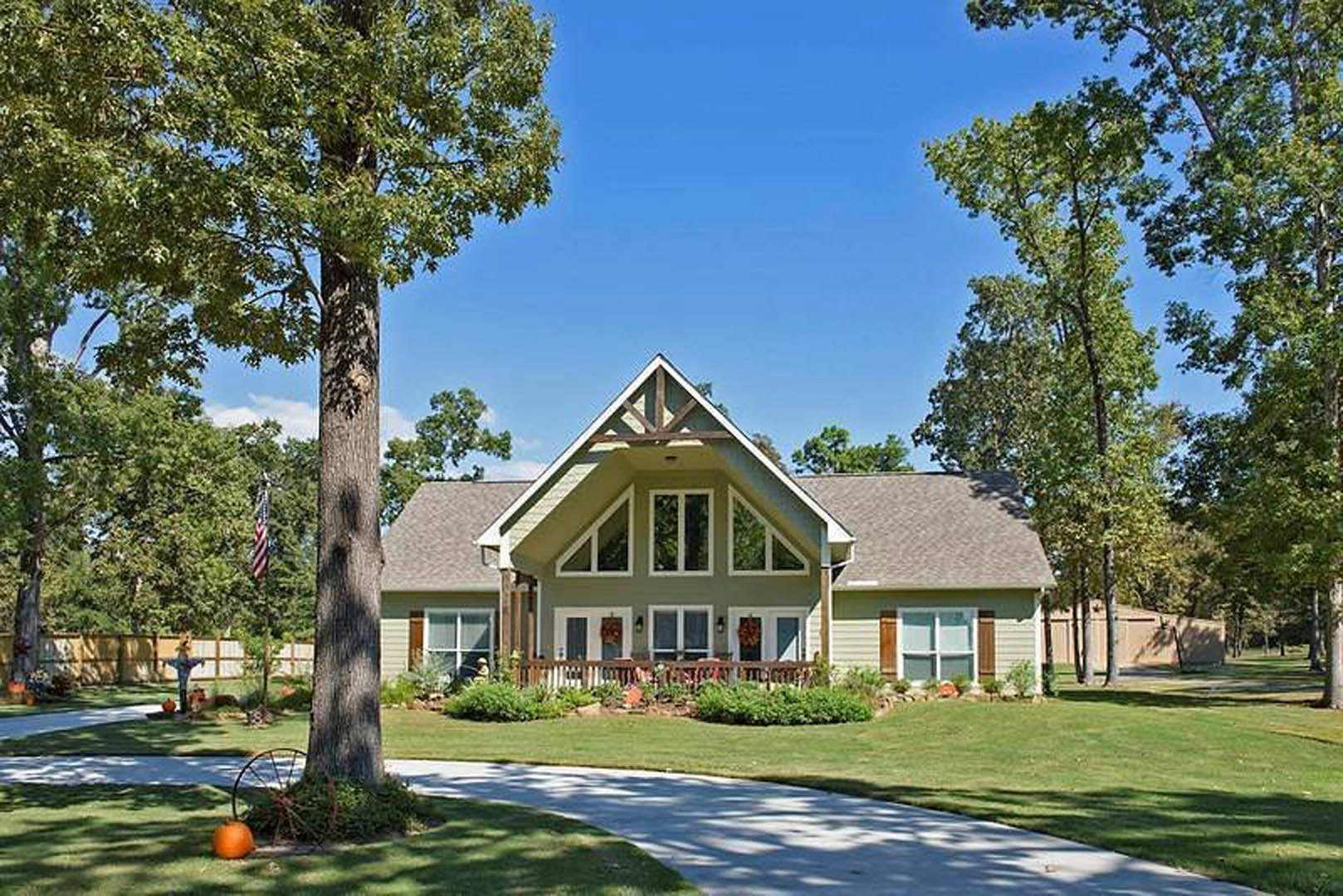 Two-story house with white siding, covered front porch, manicured lawn, mature trees, and a paved driveway bordered by bushes