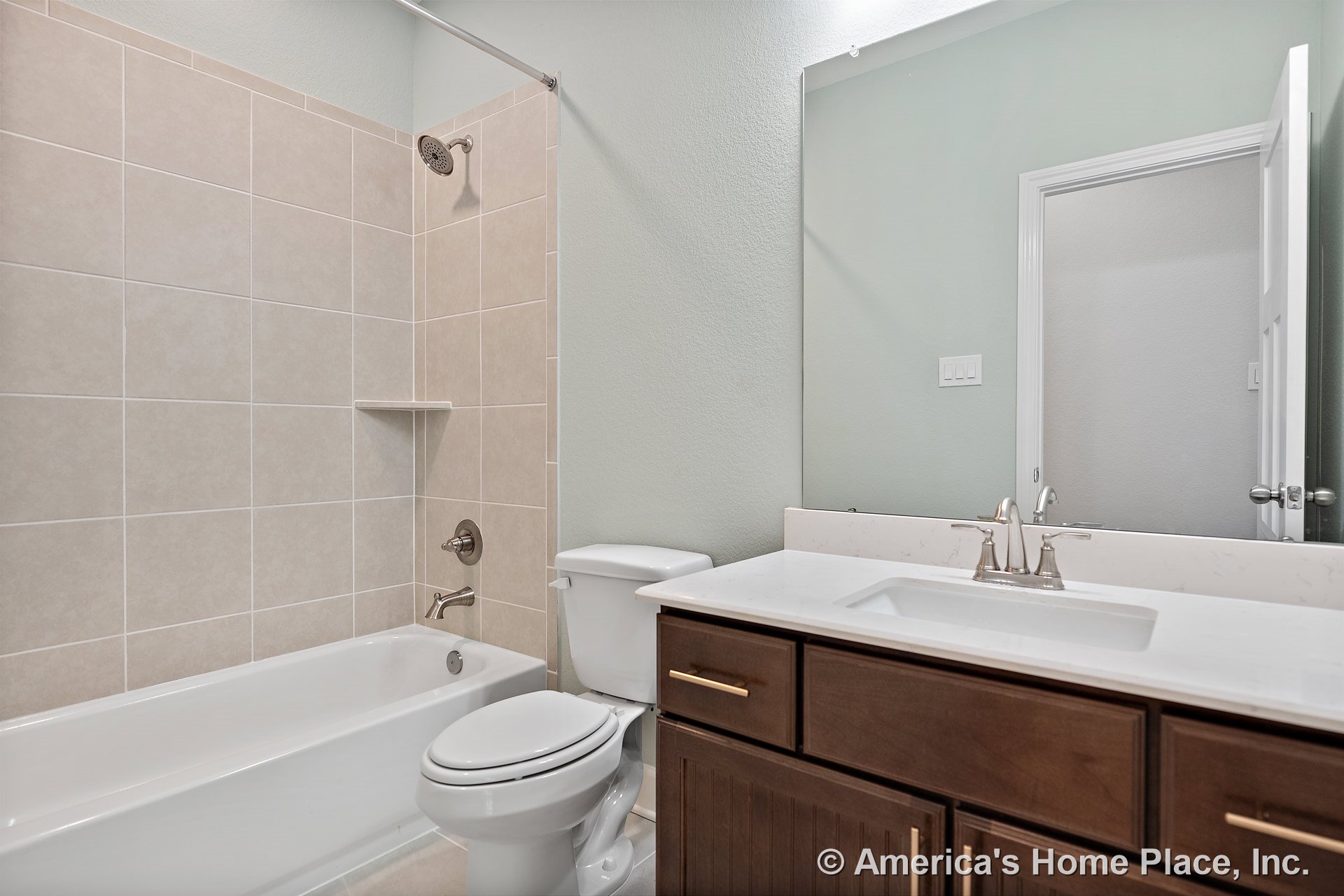 Tiled shower-tub combo with beige wall tile and built-in shower shelf, white bathtub, dark wood vanity with quartz countertop, large wall mirror, chrome faucet, and adjacent toilet
