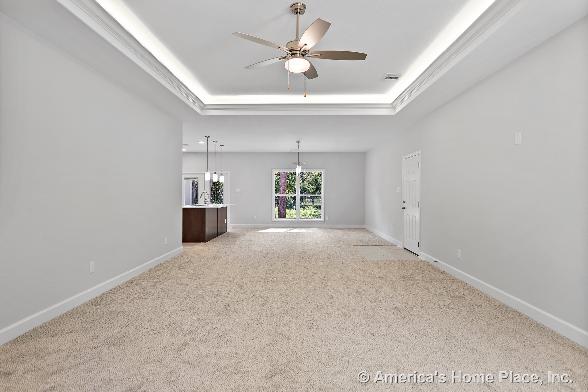 Tray ceiling with recessed lighting and ceiling fan above carpeted living area, open to kitchen with pendant lights over island, large window with backyard view, white baseboard
