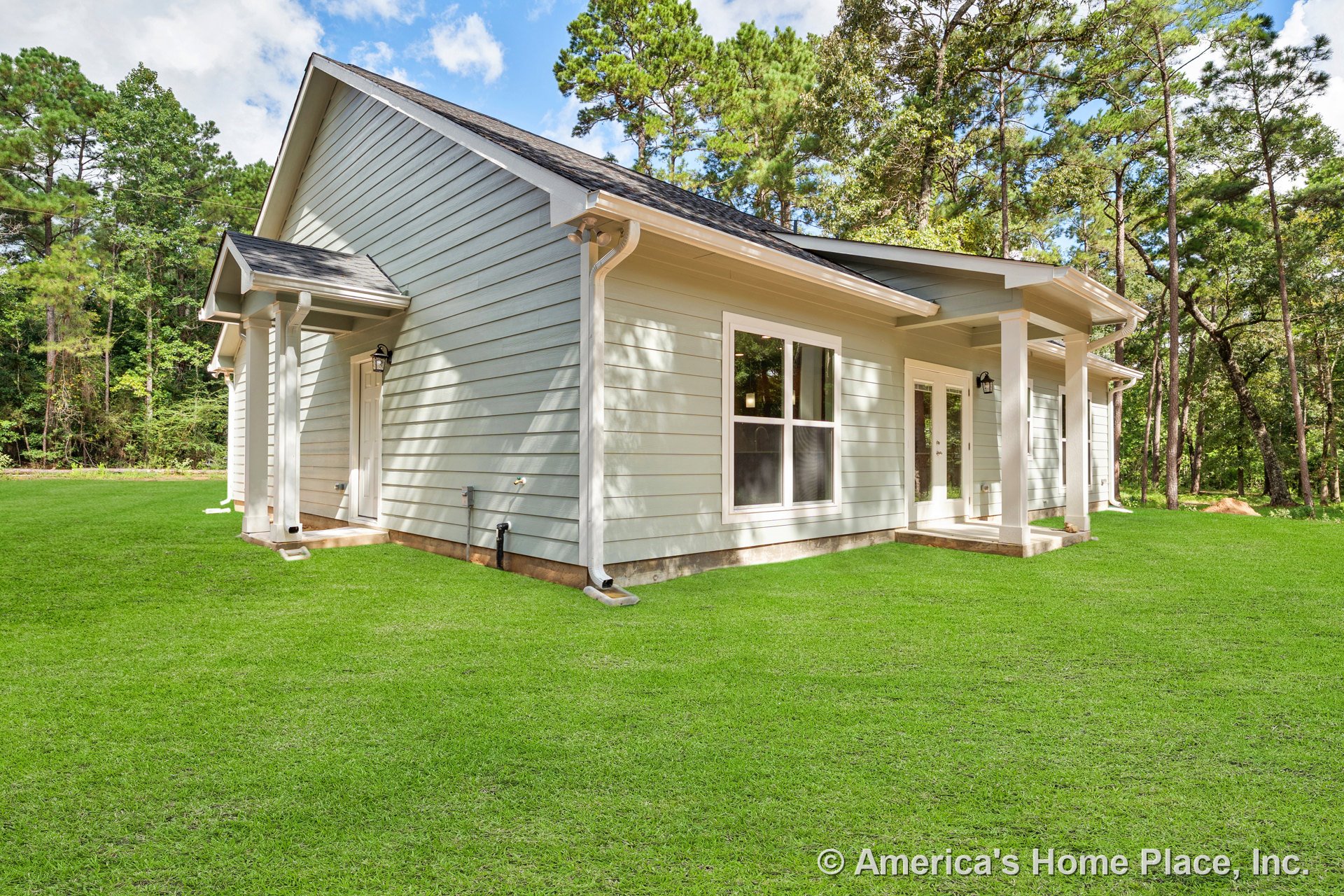 Light blue horizontal lap siding, large double windows with white trim, covered porch supported by columns, glass-panel exterior doors, white gutters, shingle roof, landscaped