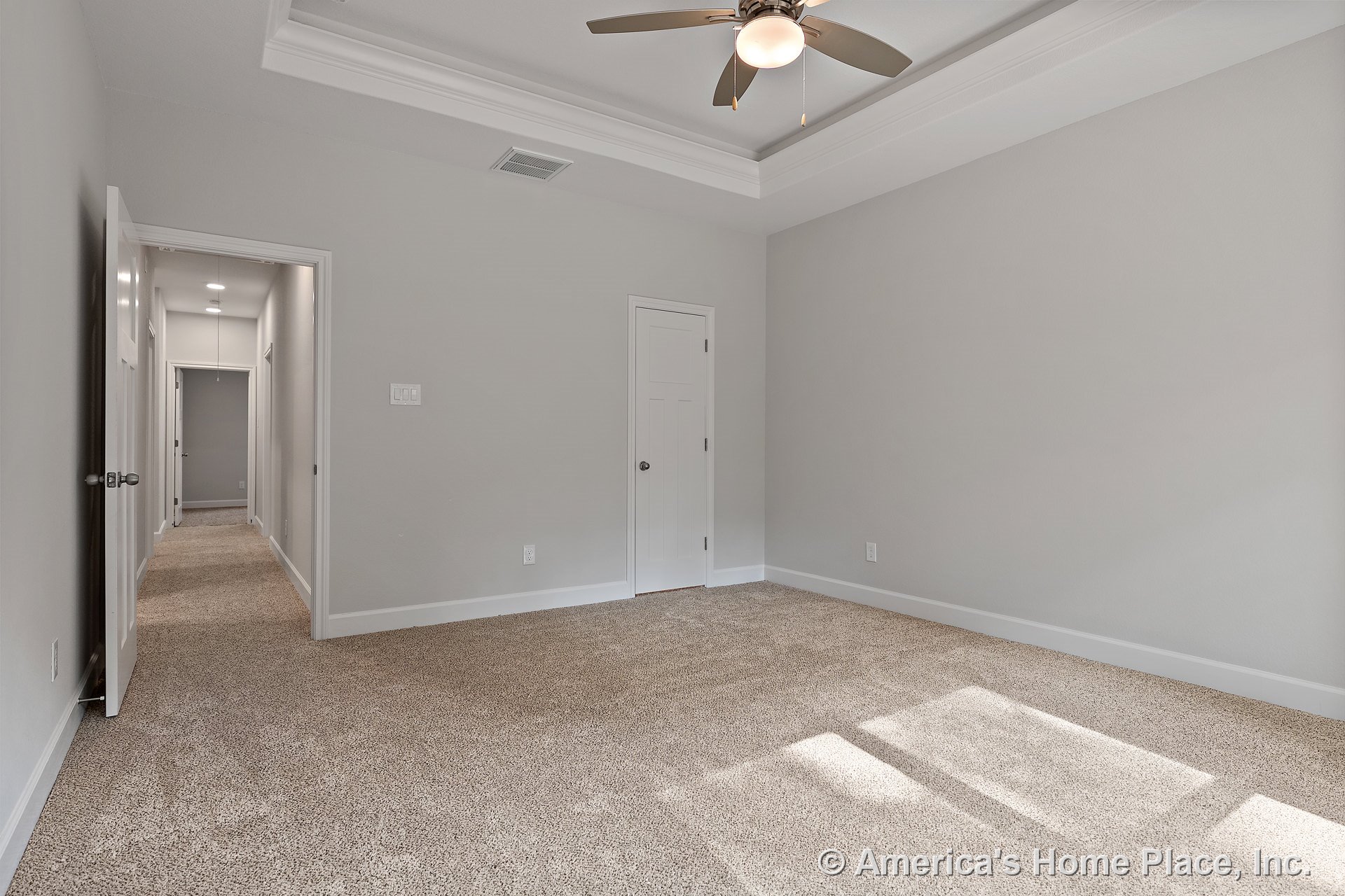 Tray ceiling with ceiling fan and light fixture, neutral carpet flooring, white baseboards, interior doors, large window allowing natural light, modern trim and paint finishes.
