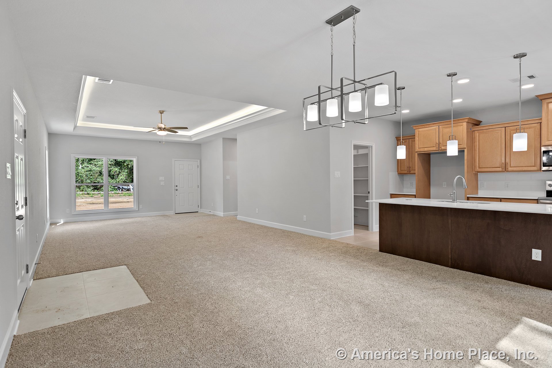 Open living area with tray ceiling and recessed lighting, large double window, carpeted flooring, kitchen island featuring quartz countertop, wood cabinetry with built-in