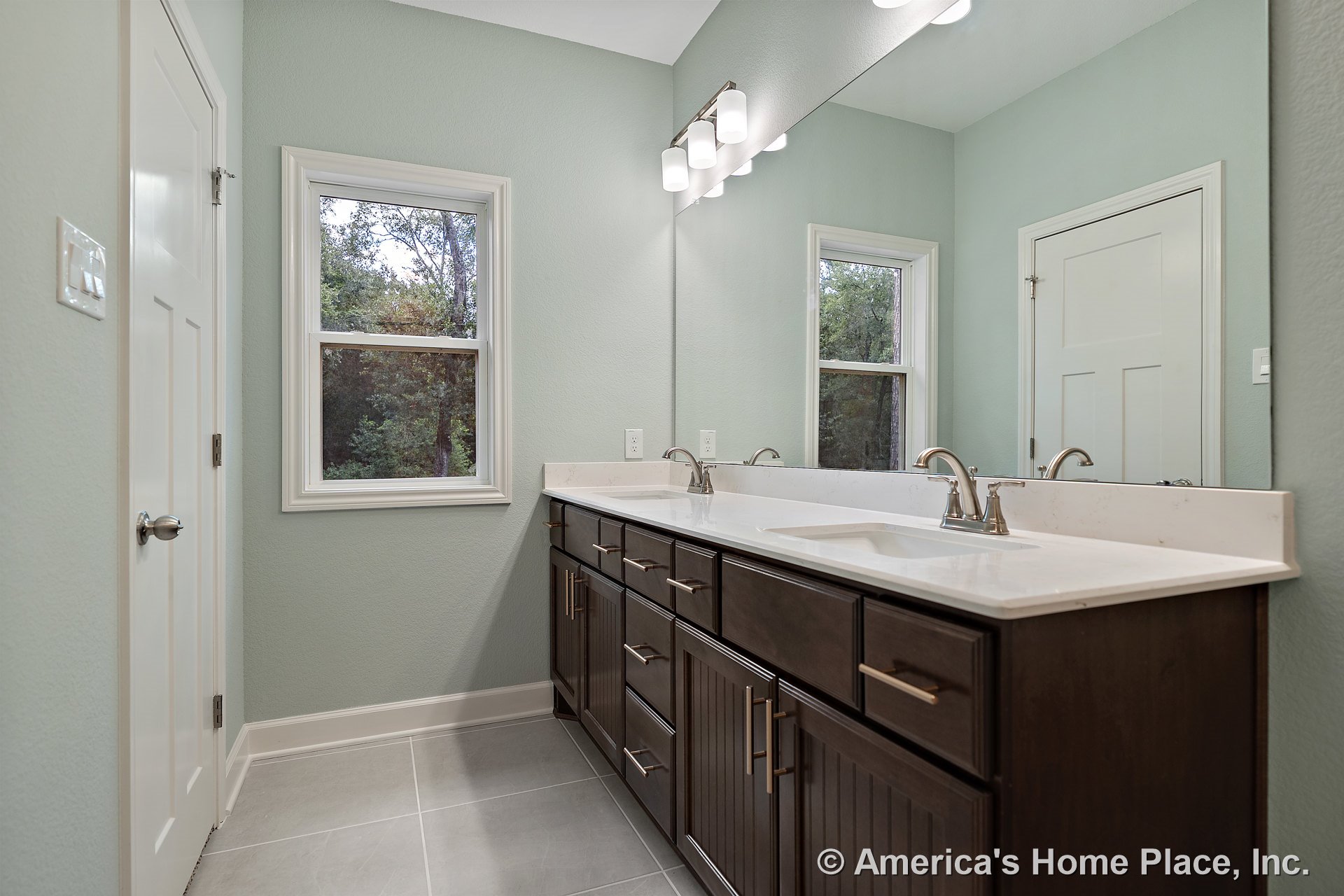 Double vanity with dark wood cabinets, quartz countertop, dual sinks, large wall mirror, modern vanity lighting, tile flooring, window trim, and white doors with built-in fixtures