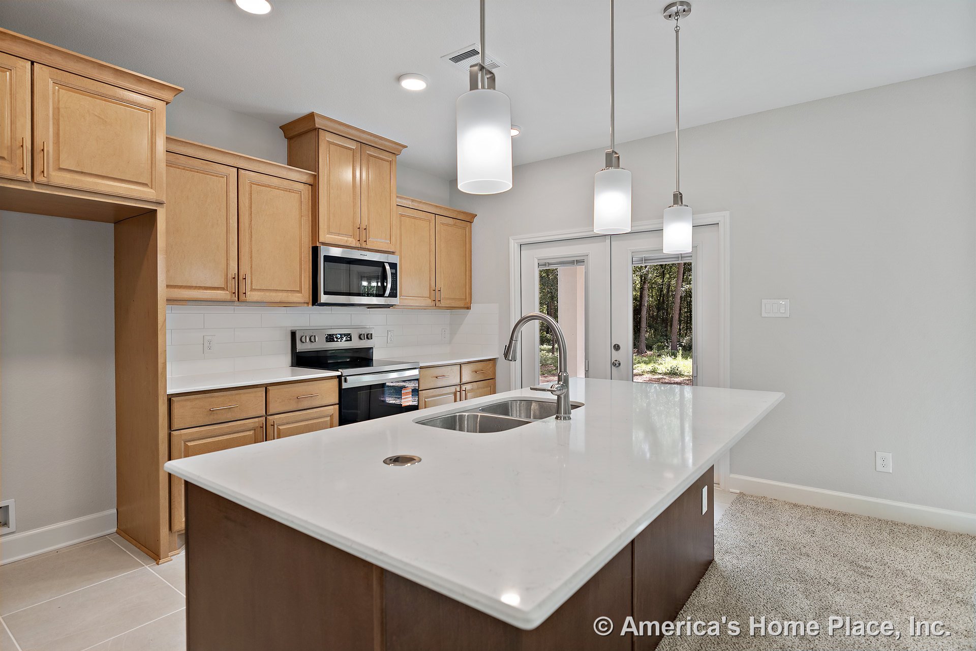 Large kitchen island with quartz countertop, pendant lights overhead, natural wood upper cabinets, stainless steel microwave and oven, white subway tile backsplash, double sink