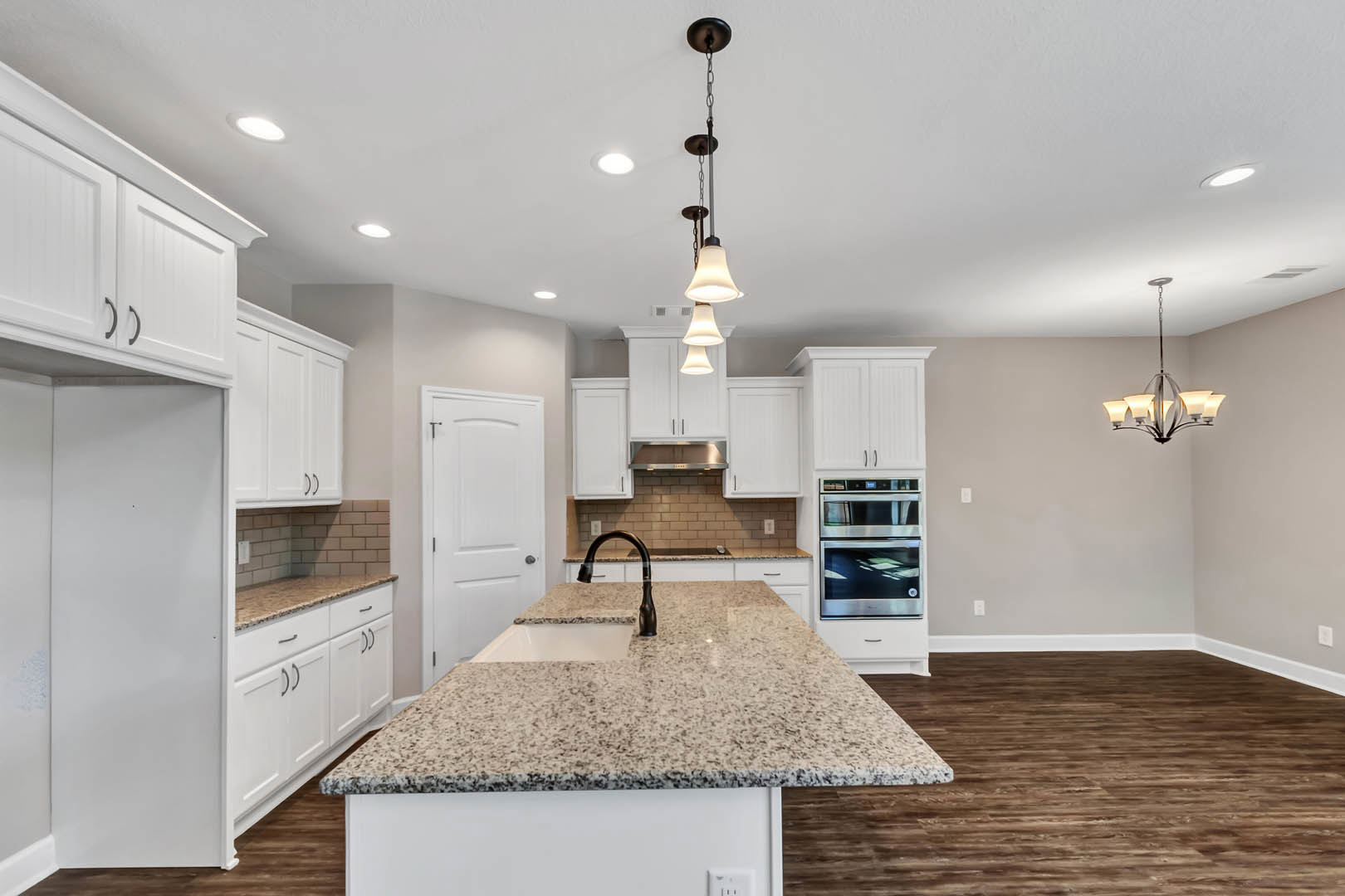 Granite kitchen island with white cabinetry, stainless steel microwave, black faucet, hanging chain light fixture, and white door with black handle