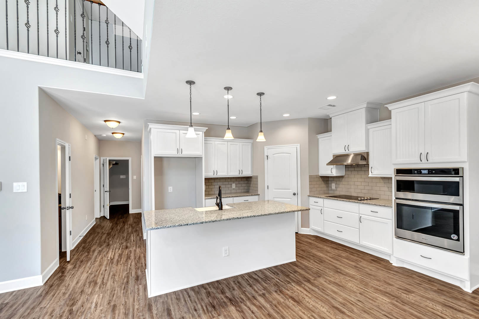 Marble island with waterfall edge, stainless steel oven with glass doors, white cabinetry, undermount sink with chrome faucet, wood flooring, glass-paneled door, light gray