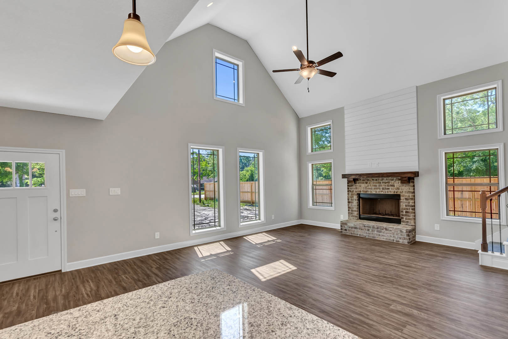 Living room with marble flooring, white walls, ceiling fan with light, stone fireplace, large windows, and white door with glass inset.