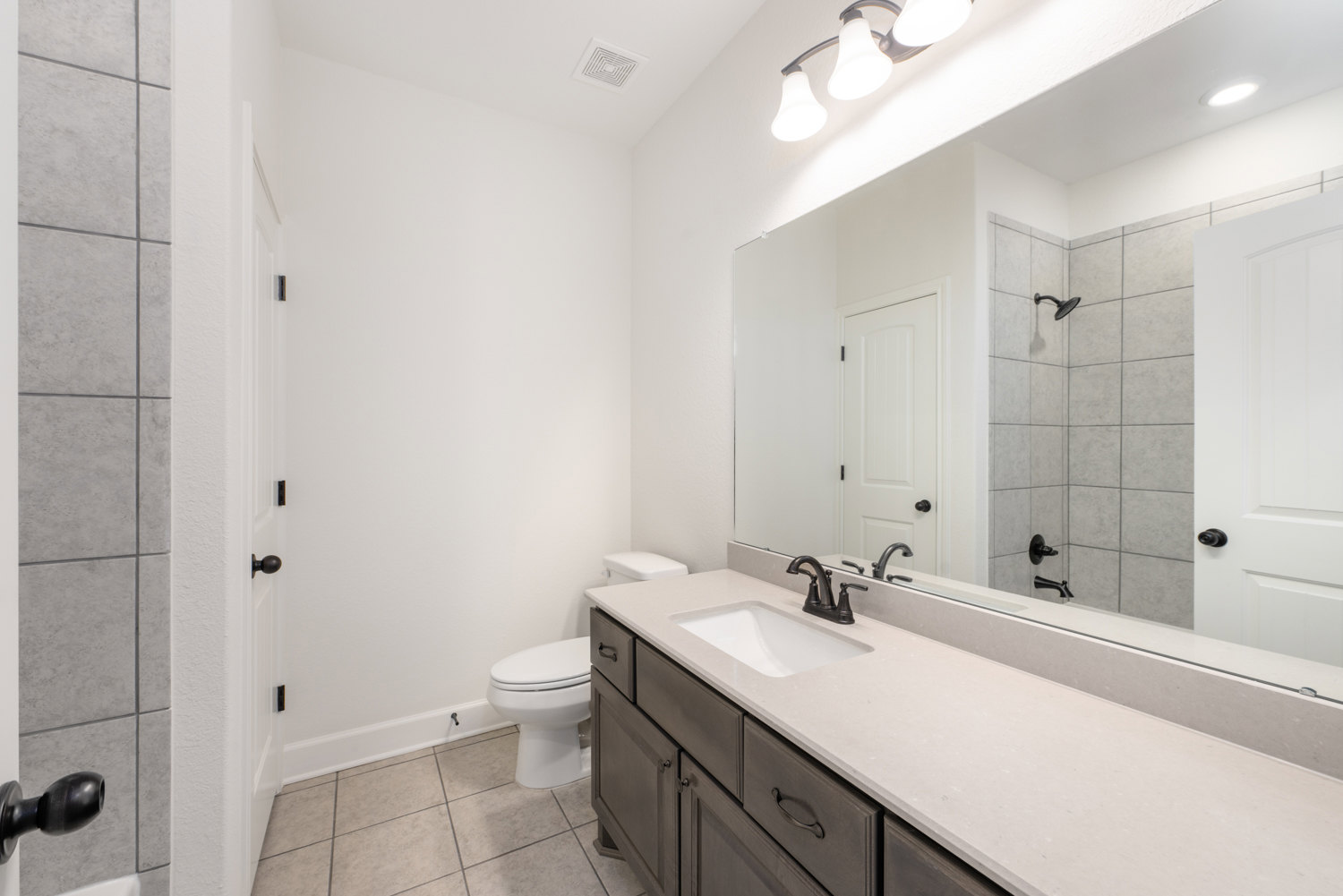 Bathroom with a wide framed mirror, white countertop and sink, matte black faucet and handles, light fixture above, white walls, and partial view of toilet.