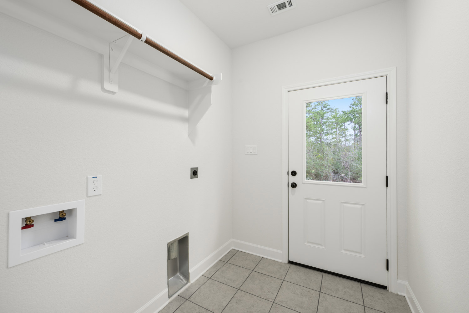 White room with smooth plaster walls, white door featuring a window, metal rack, tile flooring, electrical outlet, and a rectangular box with two plumbing valves; window reveals