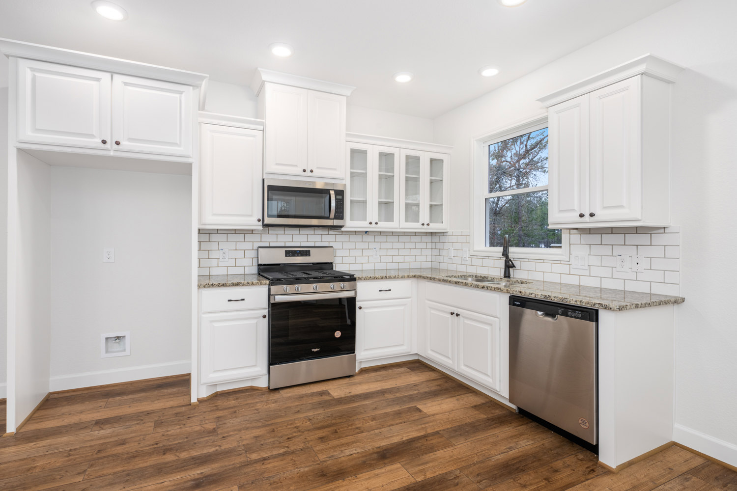 White shaker cabinets, stainless steel dishwasher and microwave, black door stove, wood flooring, light countertops, neutral walls