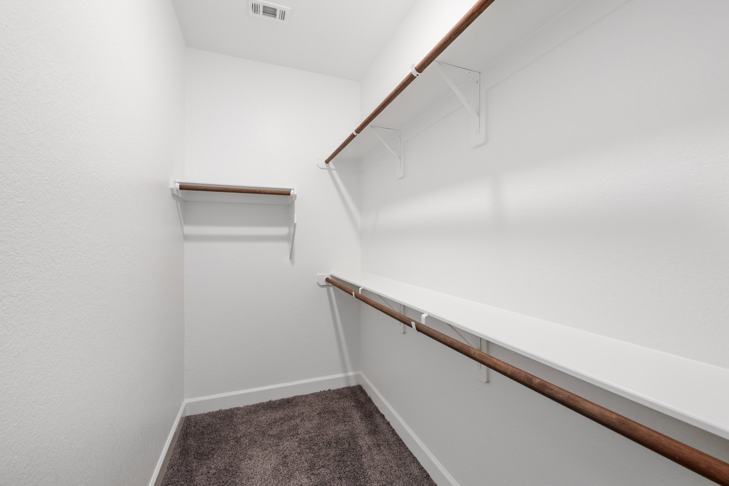 White walk-in closet with built-in shelves, wooden hanging bar, plush carpet flooring, and vent on the ceiling.