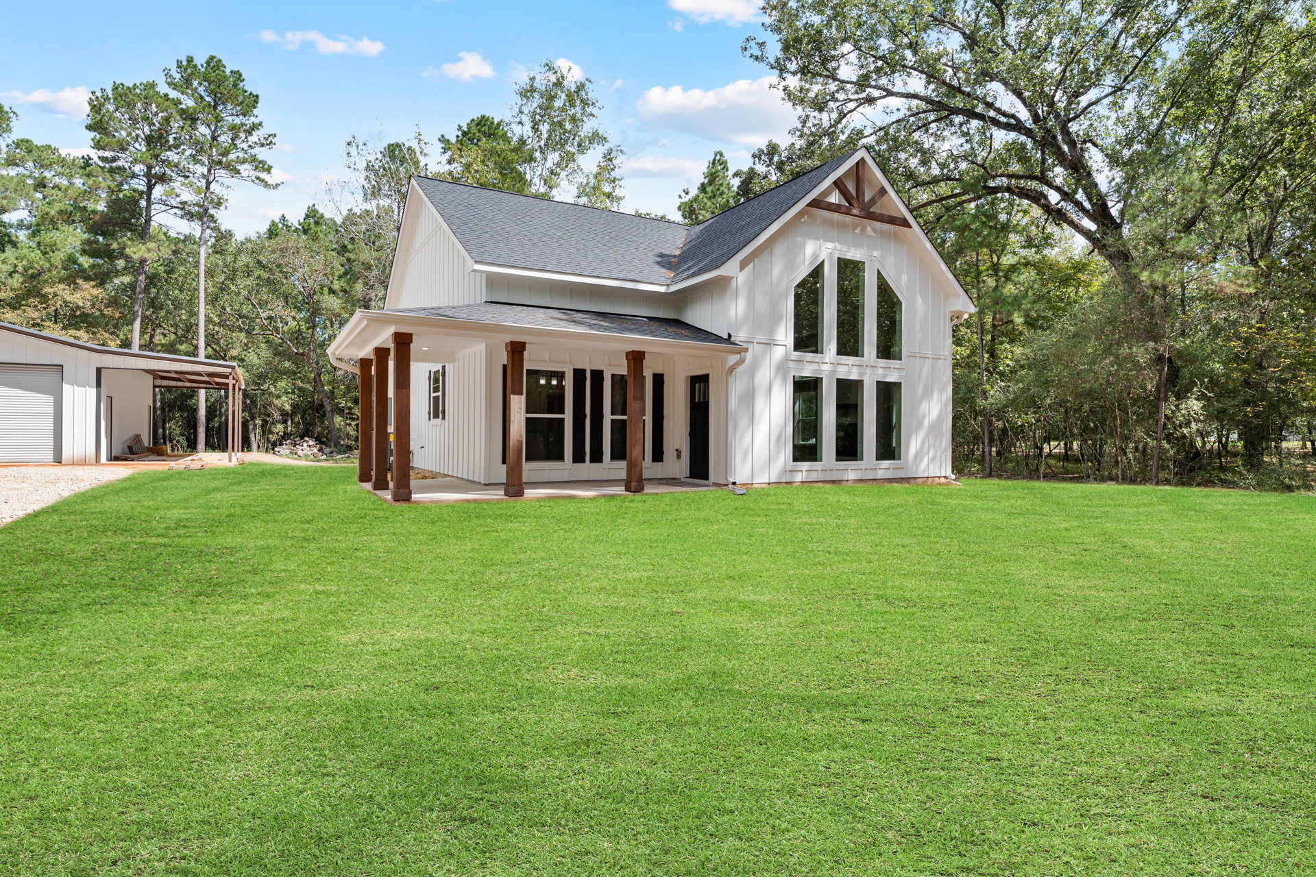White house with black door and brown pillars, green lawn in front, trees in background, close-up window visible