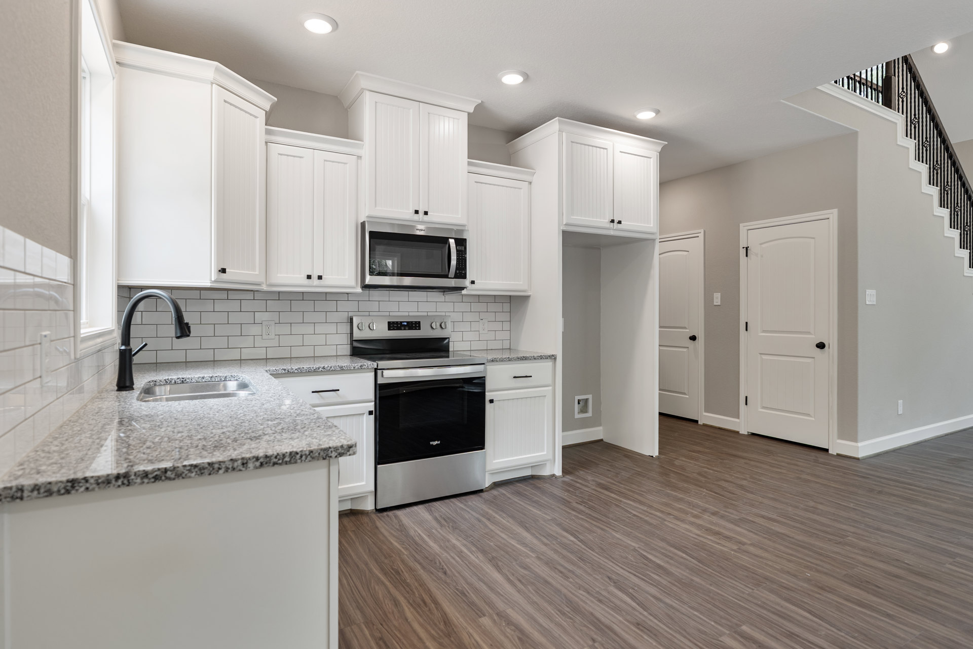 White shaker cabinets, stainless steel stove and microwave, wood plank flooring, white doors with black hardware, quartz countertop