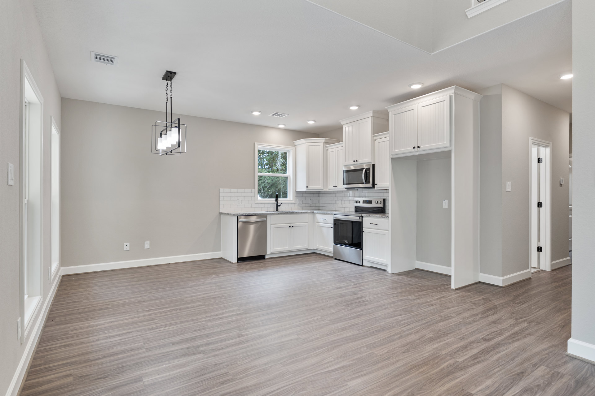 Open kitchen and dining area featuring hardwood floors, white cabinetry, stainless steel appliances including microwave and dishwasher, large window with view of trees, and modern