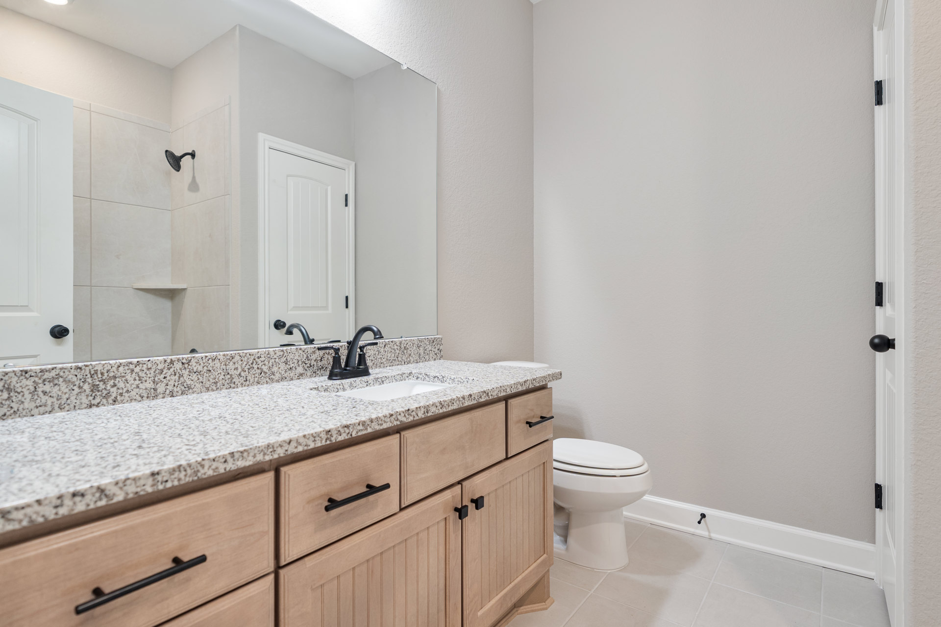 Bathroom with white toilet, white shaker cabinets, quartz countertop, undermount sink, black metal towel bar, white door with black hinges, light gray tile floor