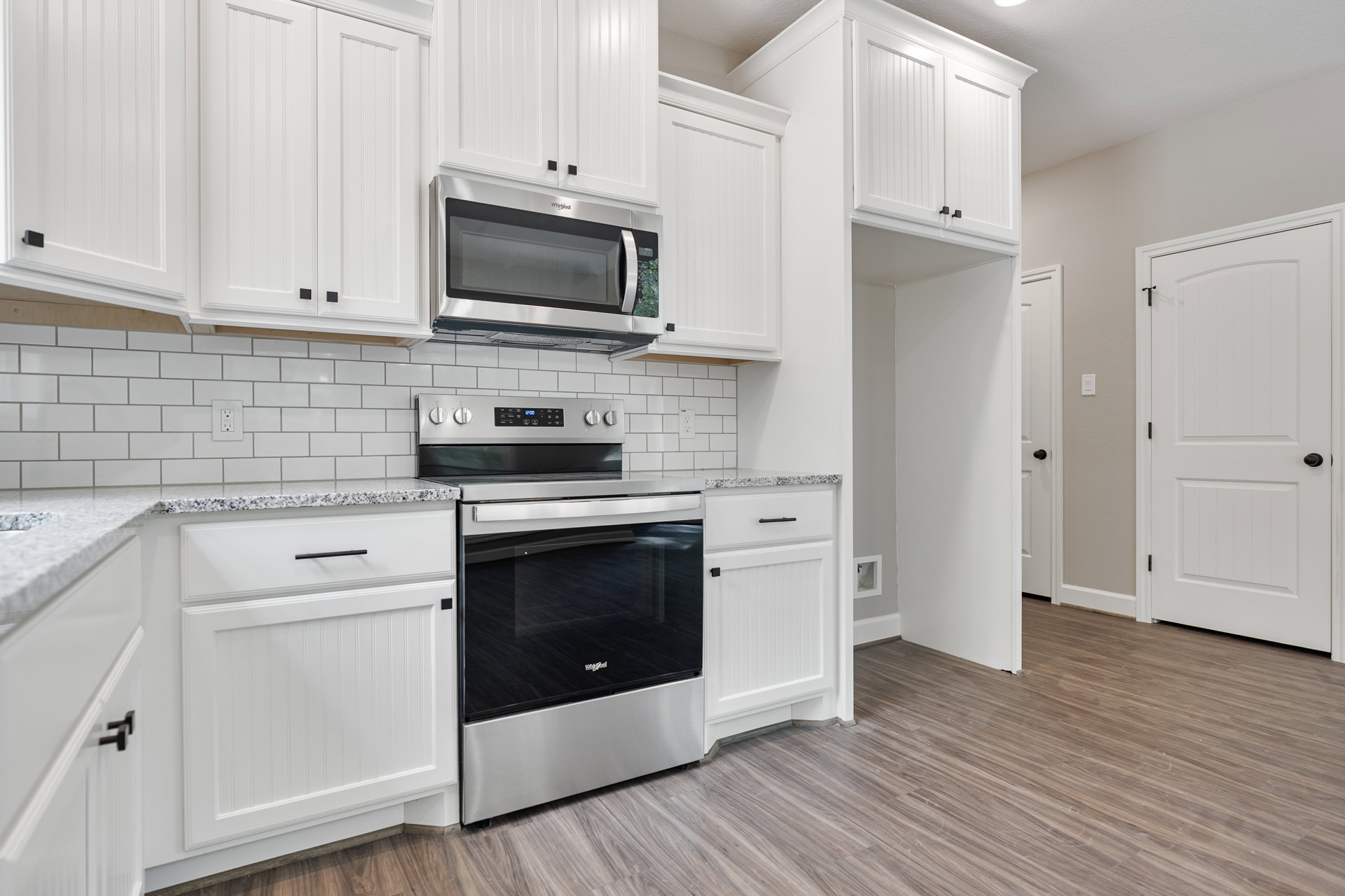 White kitchen cabinets with black handles, stainless steel oven with black glass door, built-in black and silver microwave above oven, light stone countertop, neutral tile