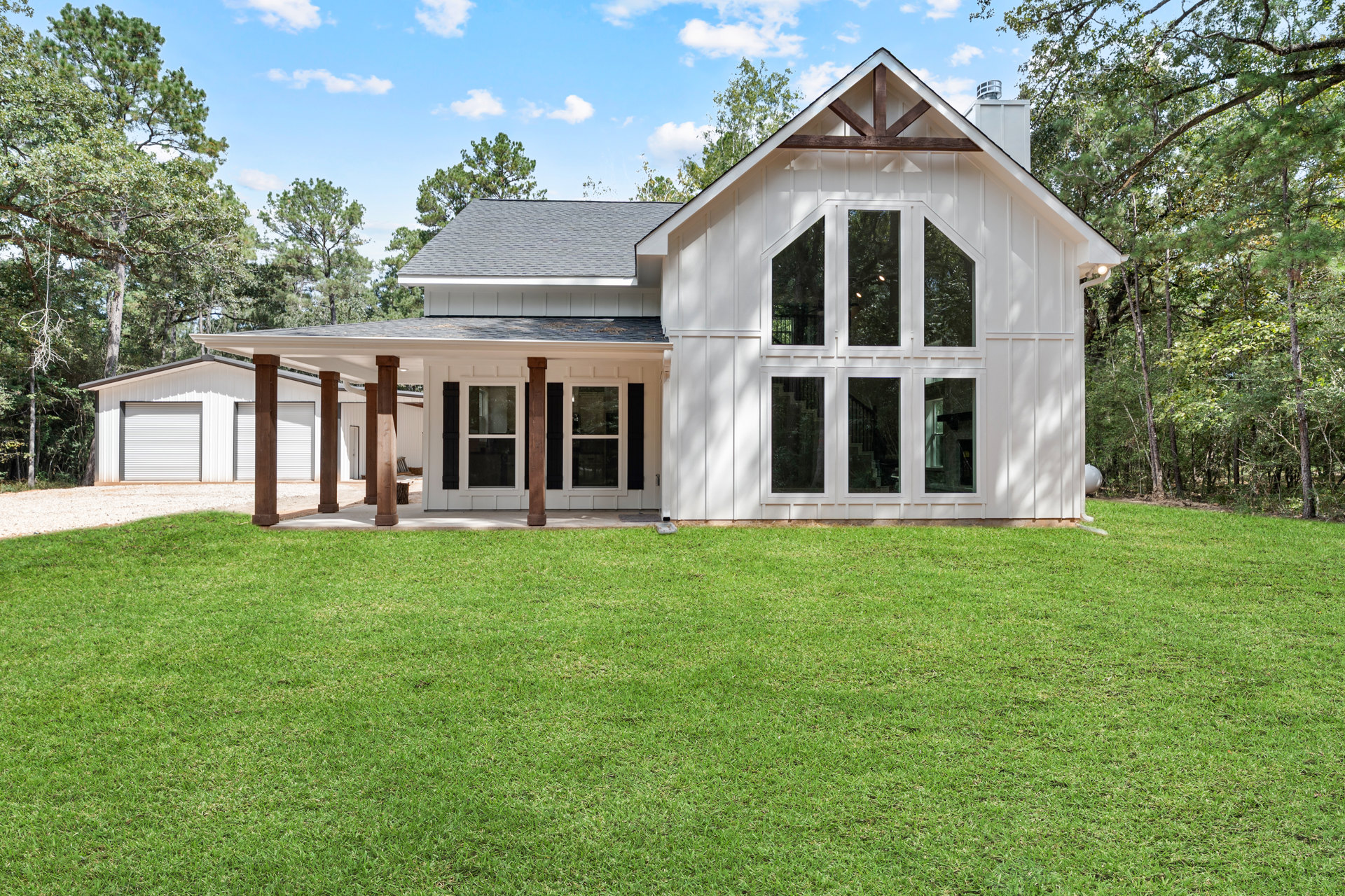 White house with brown pillars and large windows, front porch overlooking green lawn, trees and cloudy sky in background