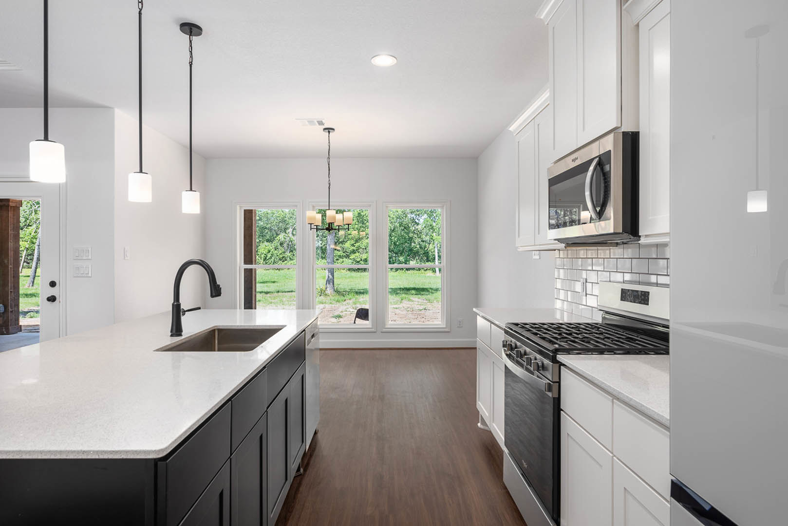 White kitchen cabinets with black stove and microwave, black faucet on white countertop, sink, and chandelier hanging from ceiling