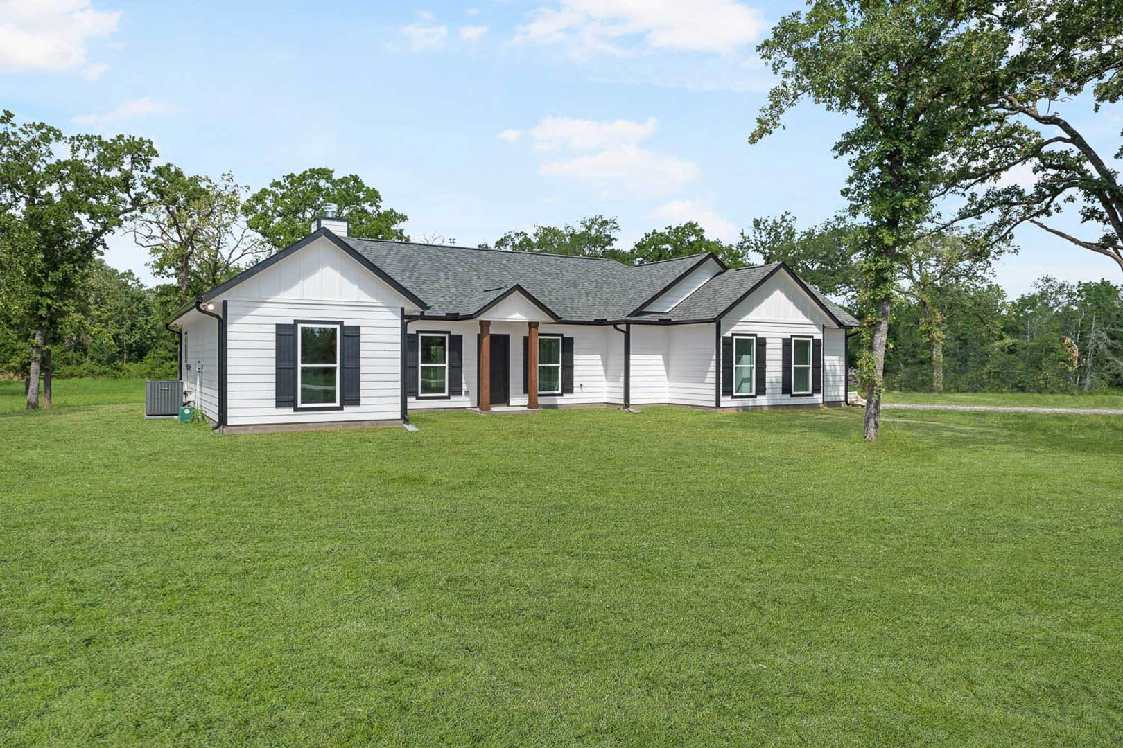 White farmhouse with black roof, white-framed windows, green lawn, and a tree beside the house; grey rectangular object sits on the grass.