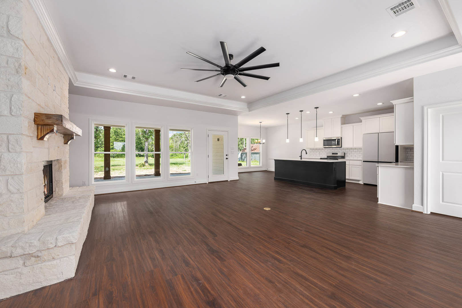 Spacious white kitchen with black island, wood flooring, ceiling fan with light, white walls, and white-framed door
