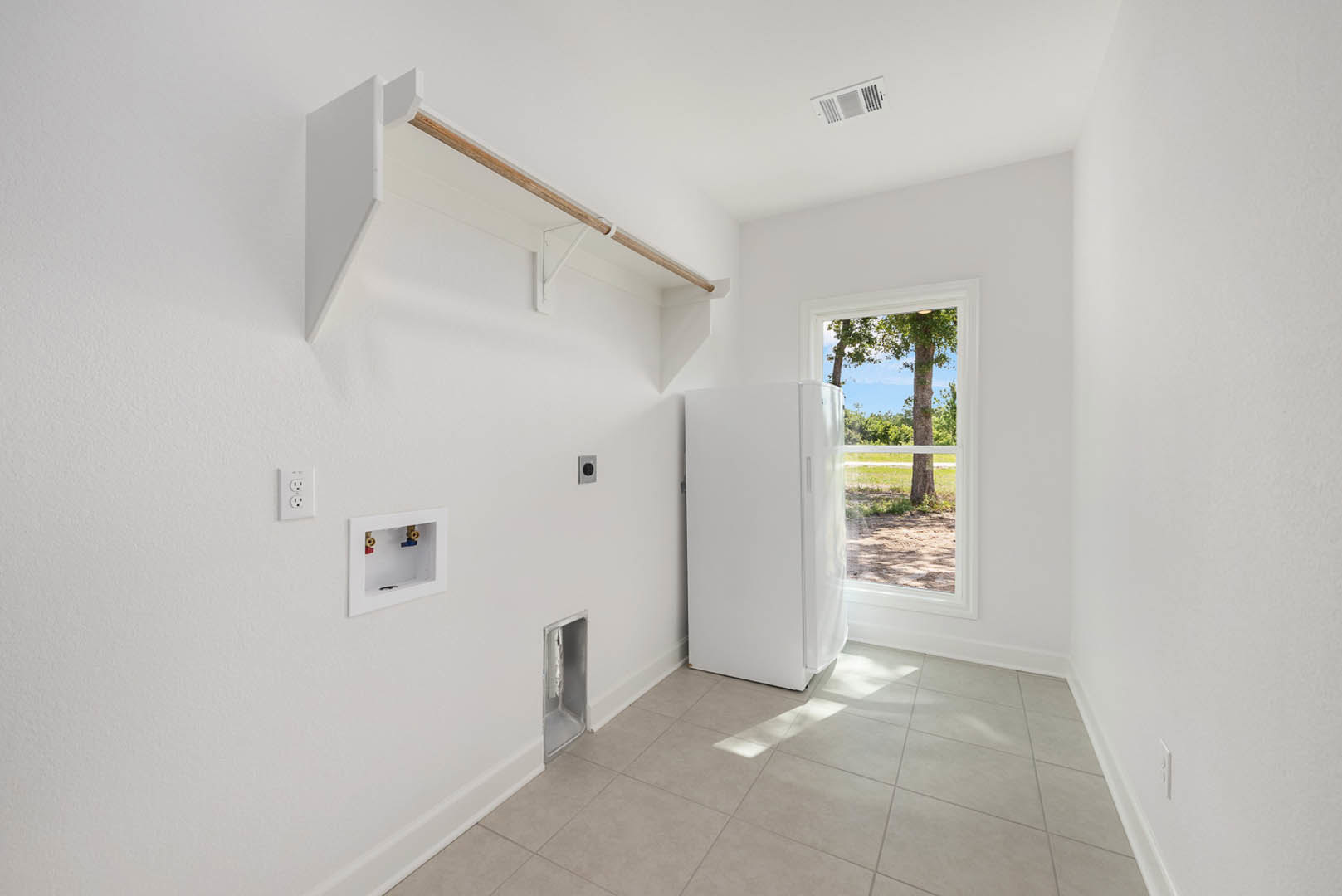White kitchen with white tile floor, white refrigerator with black handle, window, white door, and white outlet on plaster wall.