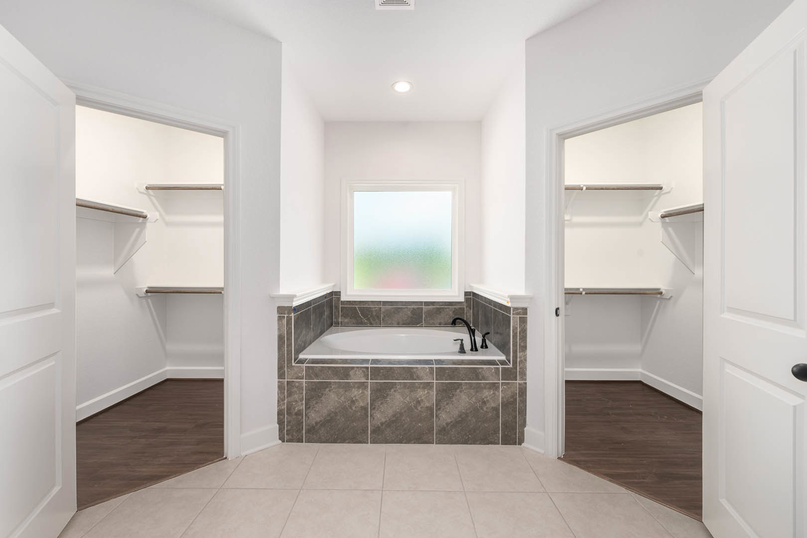 Bathroom with freestanding bathtub, two walk-in closets, dark wood flooring with white trim, tile accents, and large window providing natural light