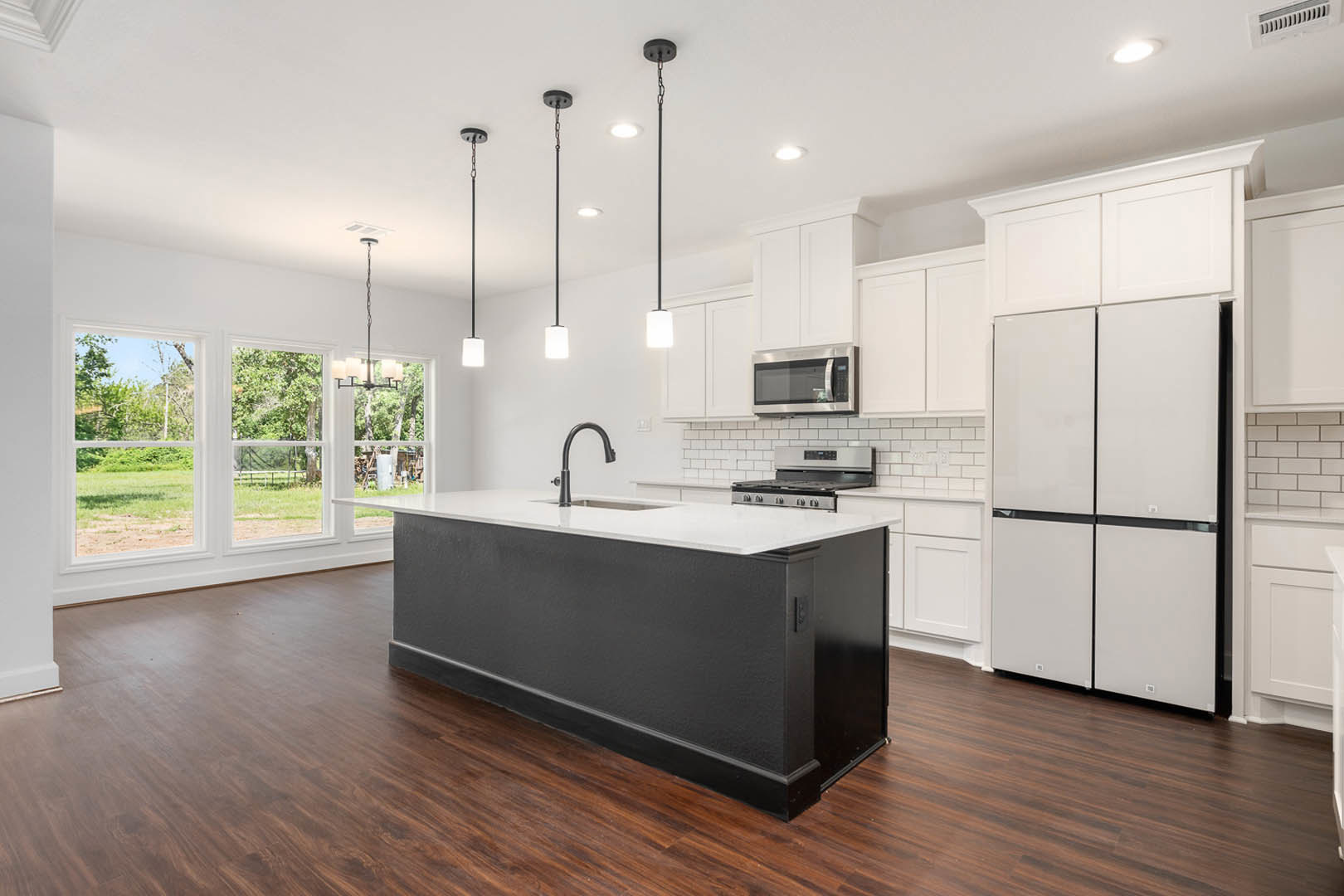 Black kitchen island with built-in sink, white upper and lower cabinets, stainless steel microwave, white refrigerator with black trim, black accent wall, white countertops, chrome