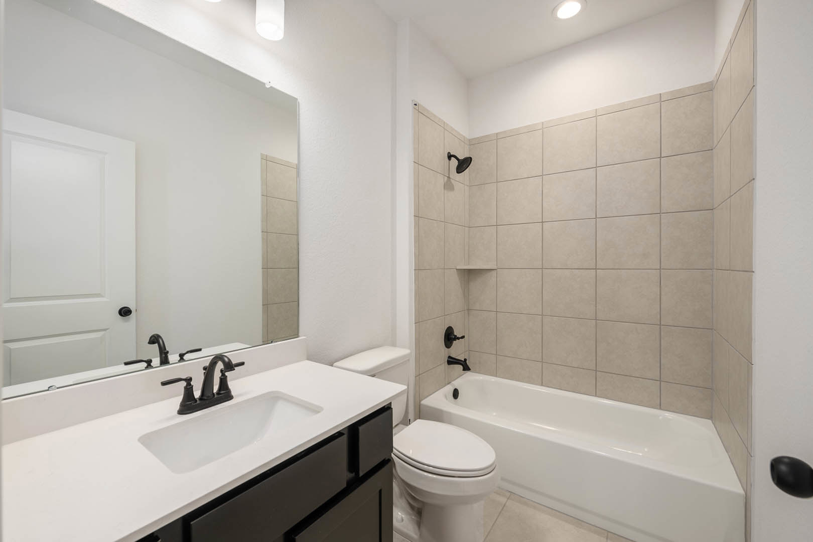 Modern bathroom featuring a white freestanding bathtub beside a closed toilet, rectangular sink with chrome faucet, light tile flooring, and neutral wall tiles