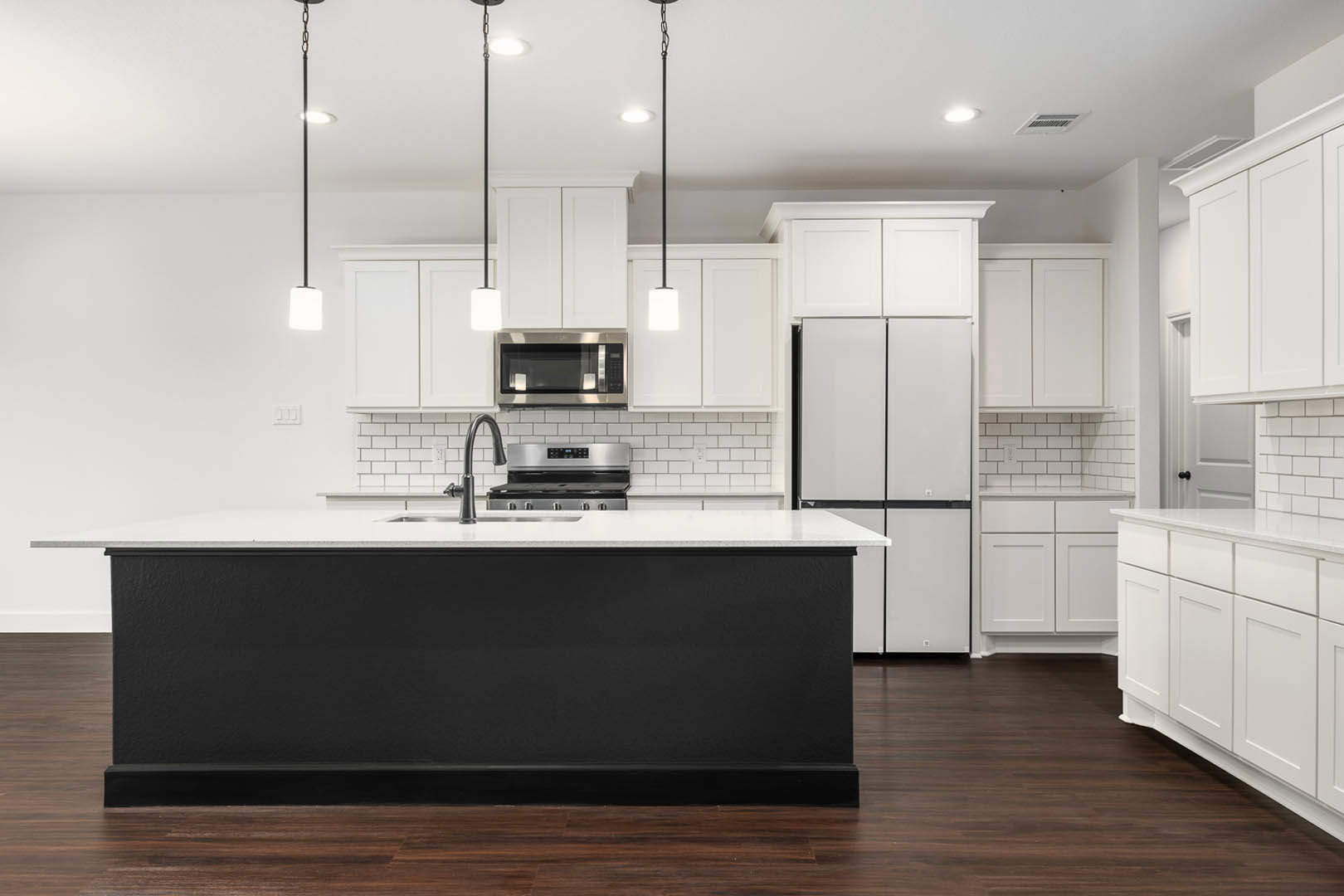White kitchen cabinets, black island with white countertop, stainless steel microwave, white pendant light with black rod, light wood flooring