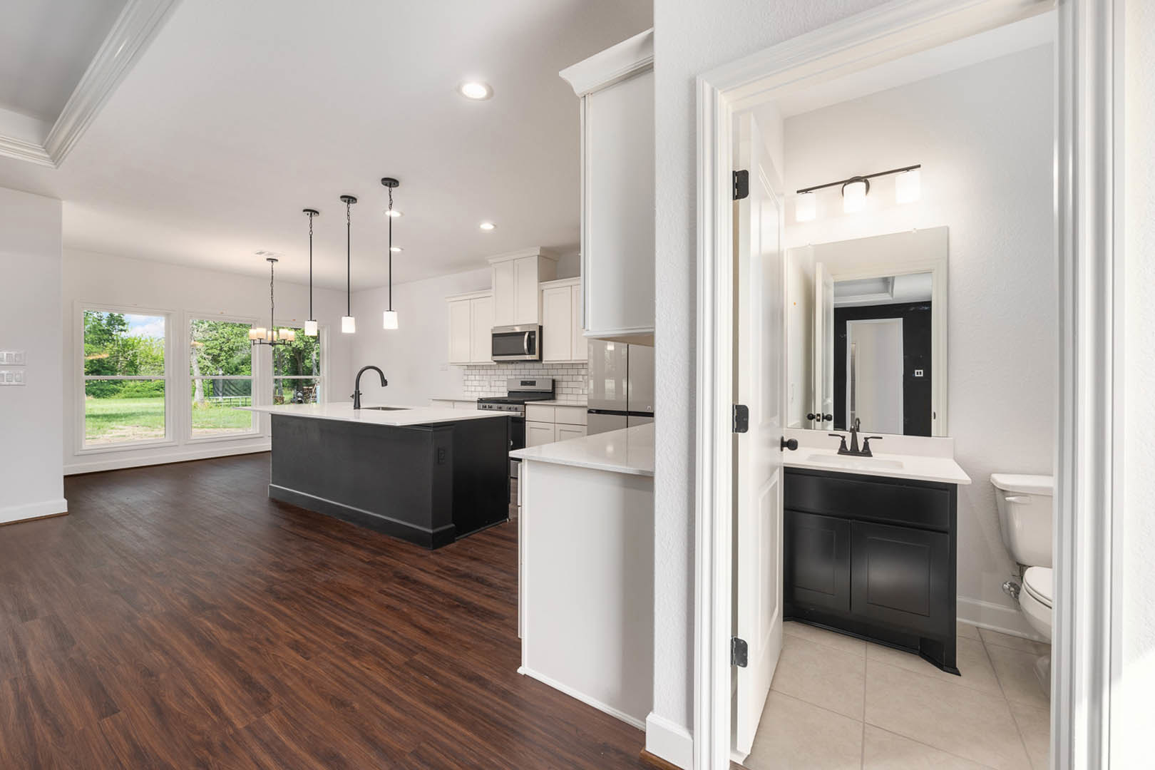 Open kitchen and living room featuring hardwood flooring, black and white kitchen island, black cabinetry, built-in microwave, white countertops with black faucet, pendant