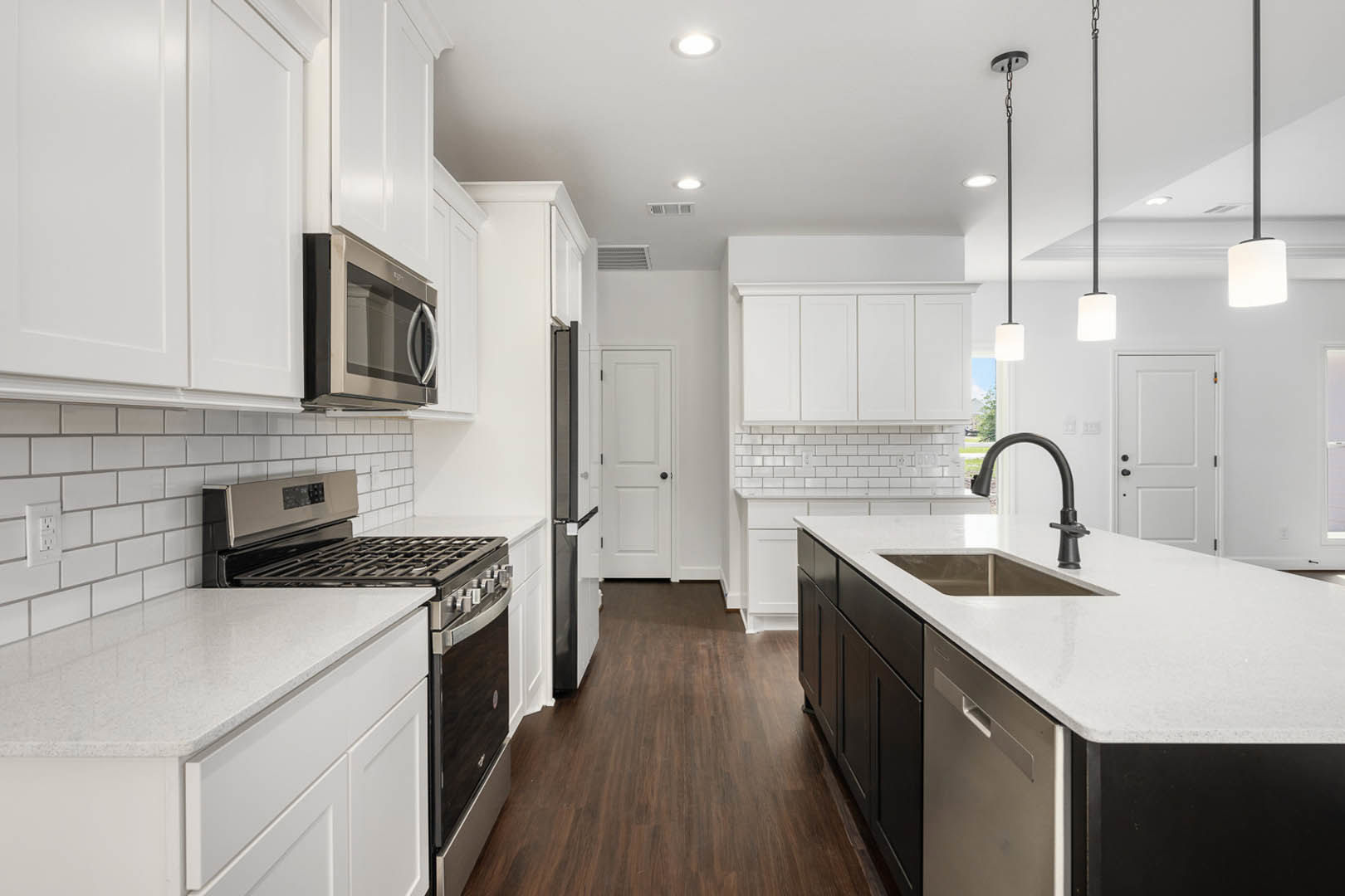 White kitchen cabinets with black appliances, including stove, oven, and microwave; tile backsplash, white countertop with stainless steel sink, white wall outlet, and white door