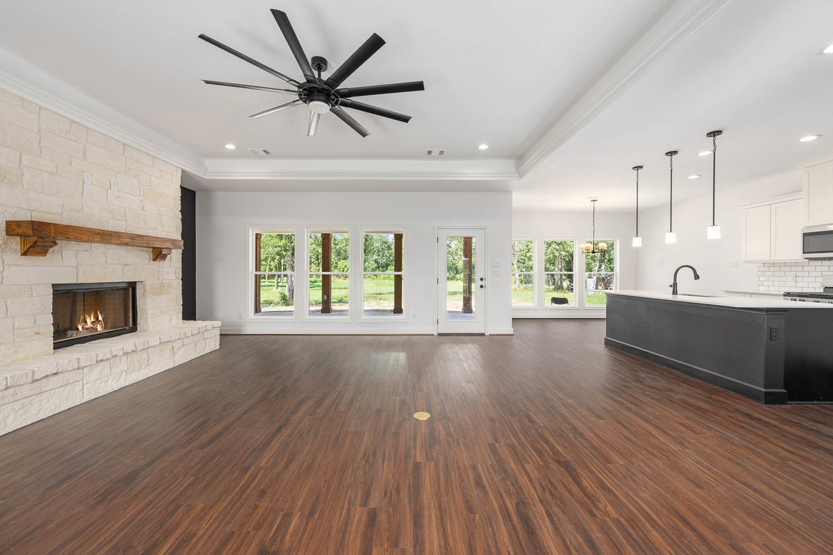 Spacious living area featuring hardwood floors with a circular inlay, stone fireplace with active fire, ceiling fan with light fixture, black and white countertops, and large