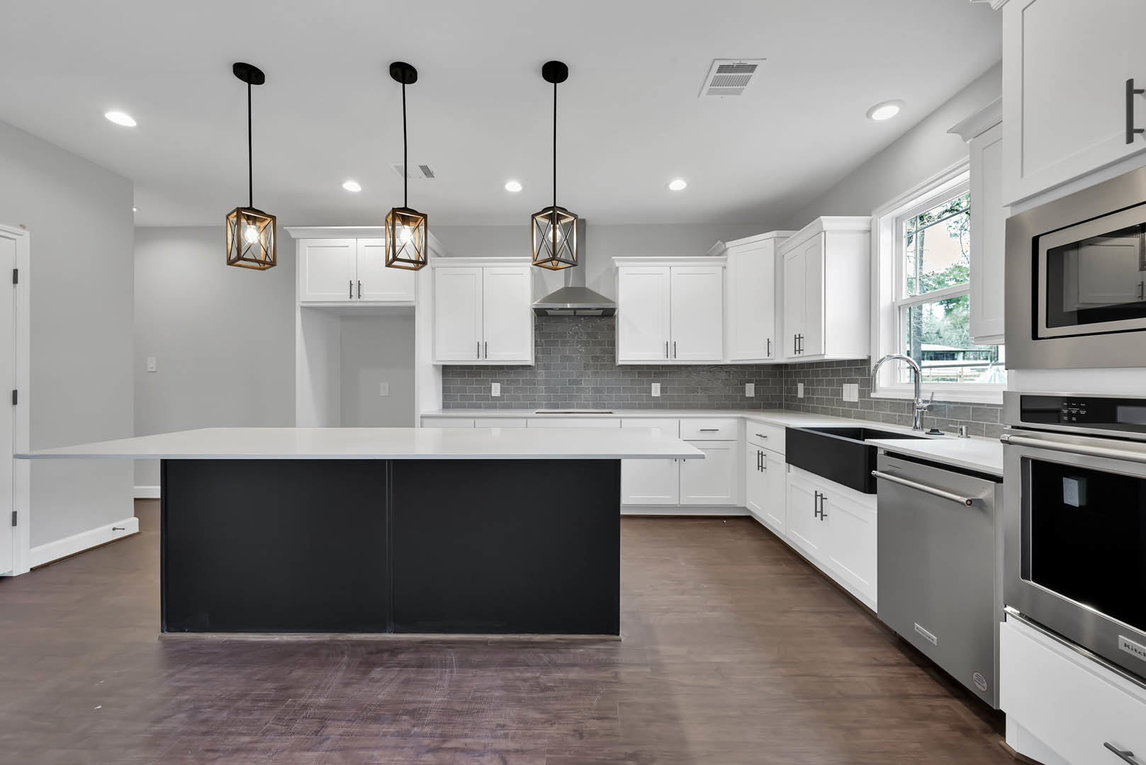 White kitchen cabinets, black island with waterfall countertop, stainless steel microwave and dishwasher, wood box pendant light with exposed bulb, light fixture above island