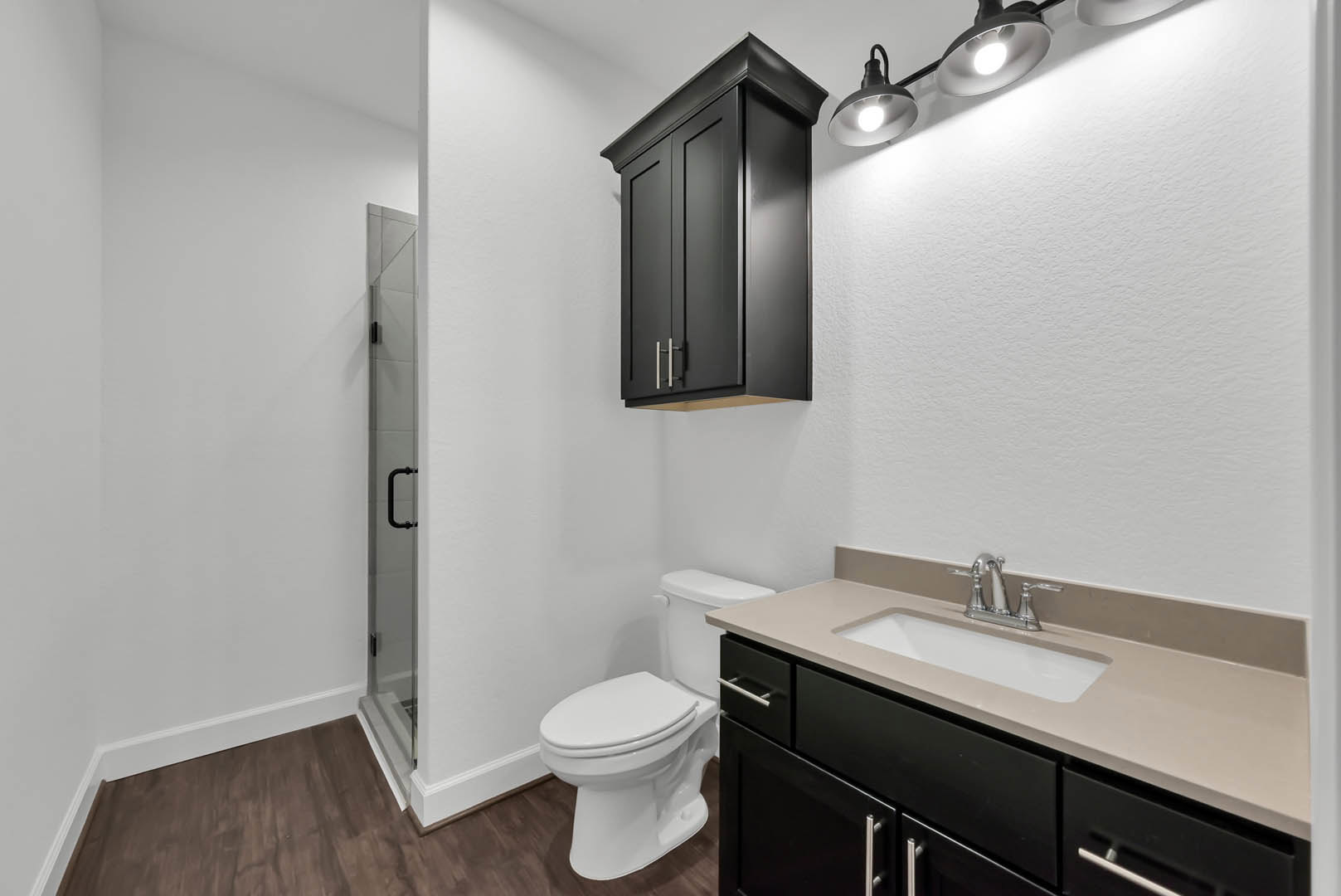 Modern bathroom with white toilet, black vanity cabinet, rectangular sink, chrome faucet, wall-mounted mirror, and light fixture above tiled wall.