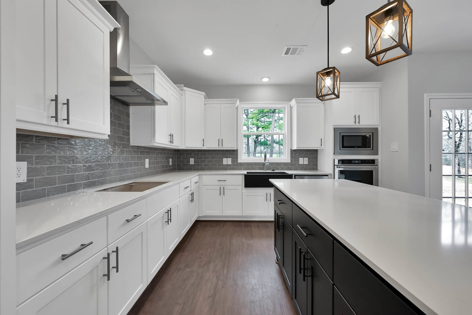 White kitchen cabinets with matte black countertops, stainless steel sink, built-in microwave with black screen, square pendant light fixture illuminated above, window overlooking