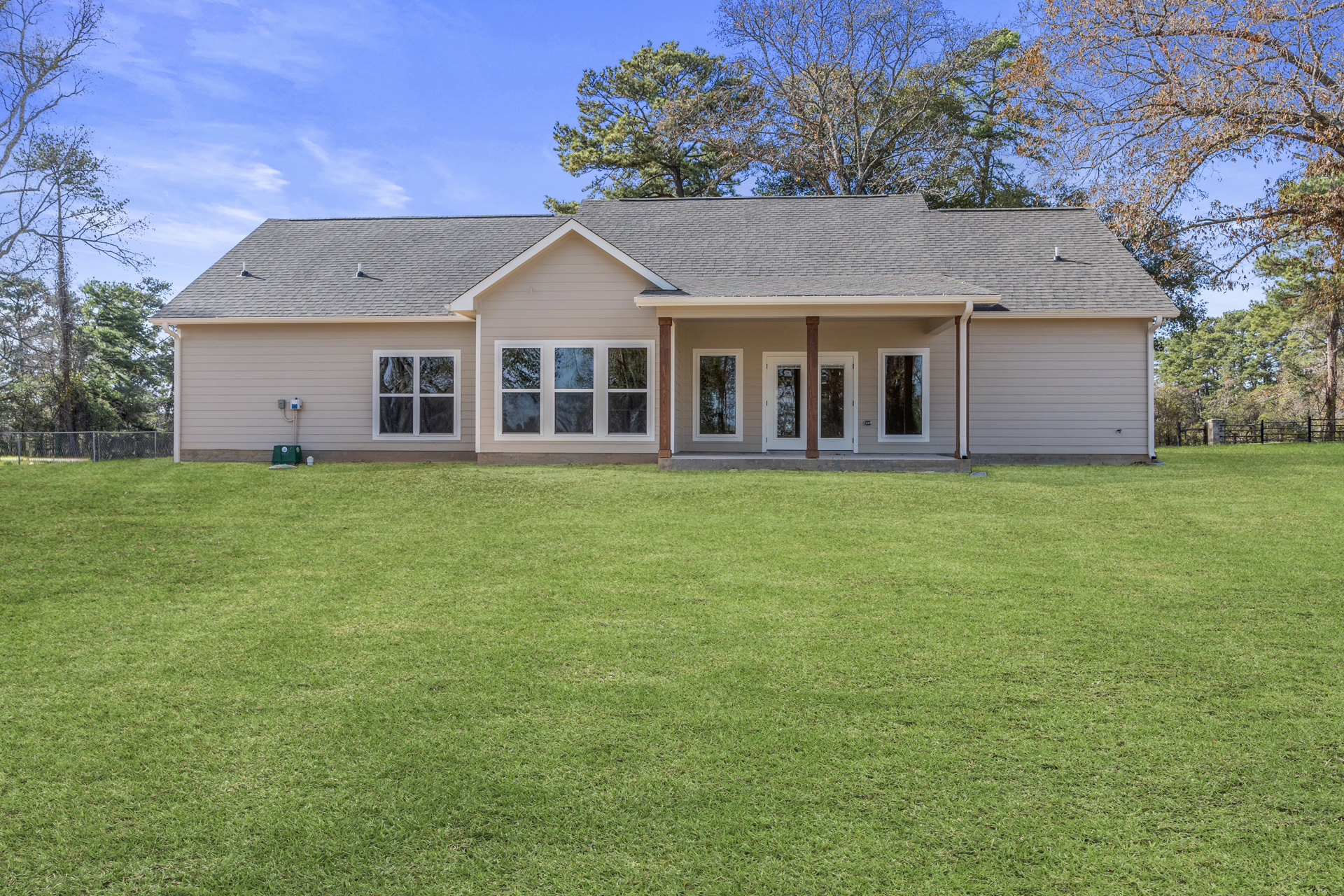 Two-story home with white siding, covered front porch, double glass-paneled doors, large windows reflecting nearby trees, and manicured green lawn