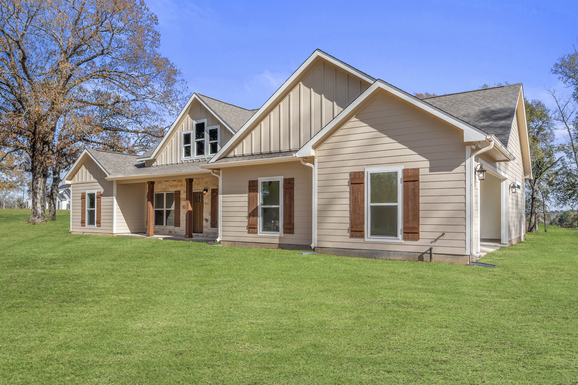 Two-story home with white-framed windows, covered porch, manicured front lawn, mature tree, and clear blue sky