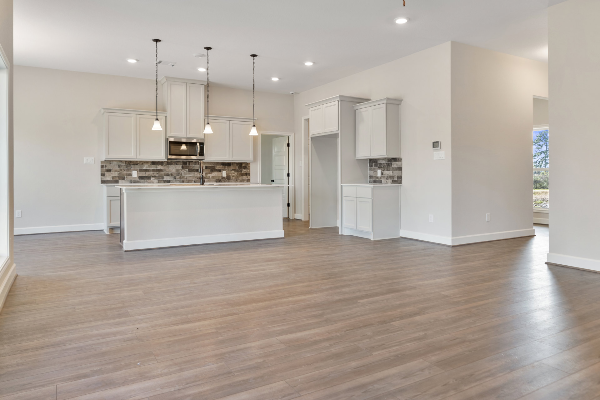 Open kitchen and living room with hardwood floors, white walls, white cabinetry, white countertop, black pendant lamp, built-in microwave with illuminated interior, open shelf