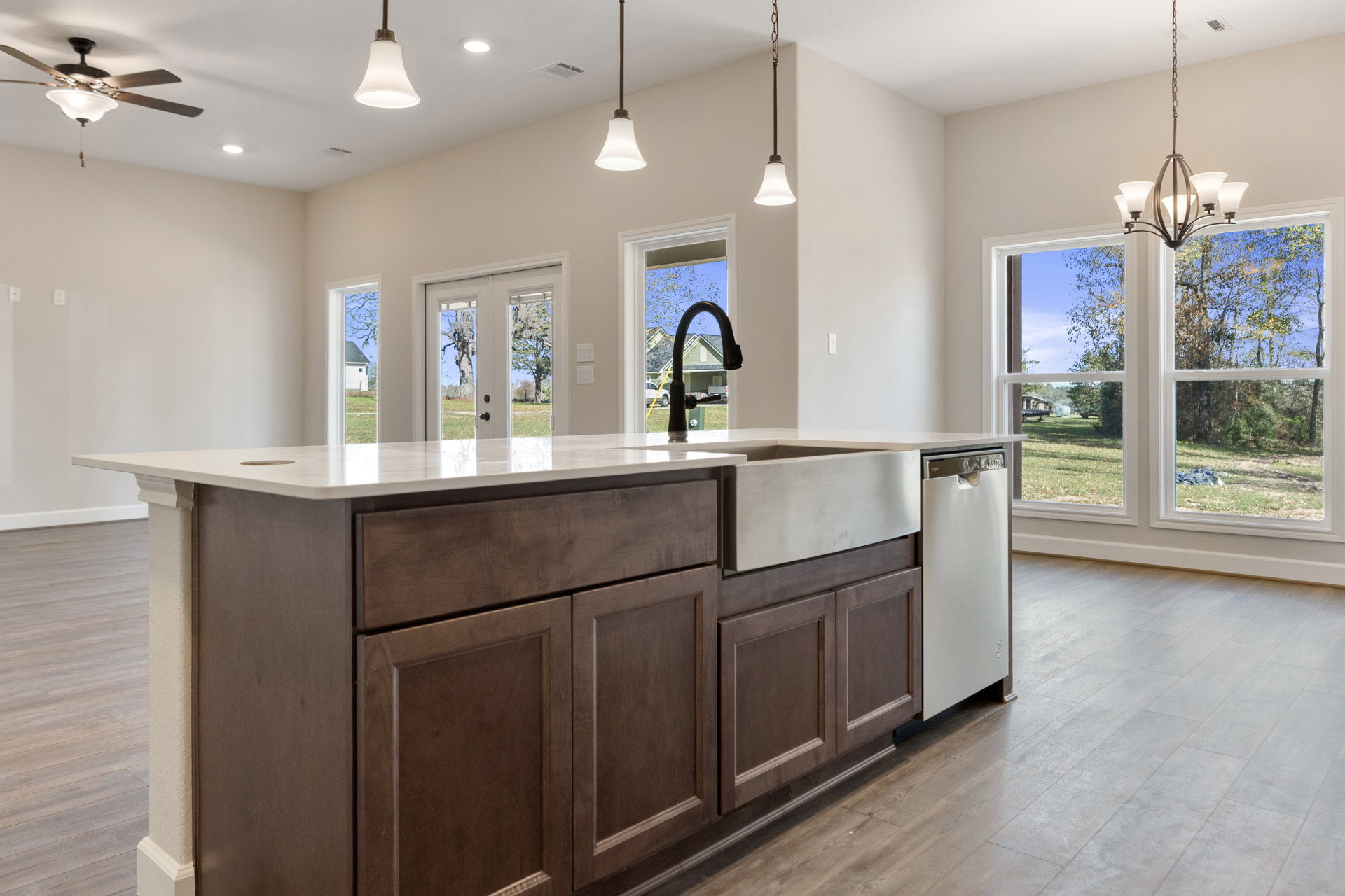 Modern kitchen featuring a central island with built-in sink and faucet, white cabinetry, brown-framed window, pendant light fixture, and light-colored countertops.