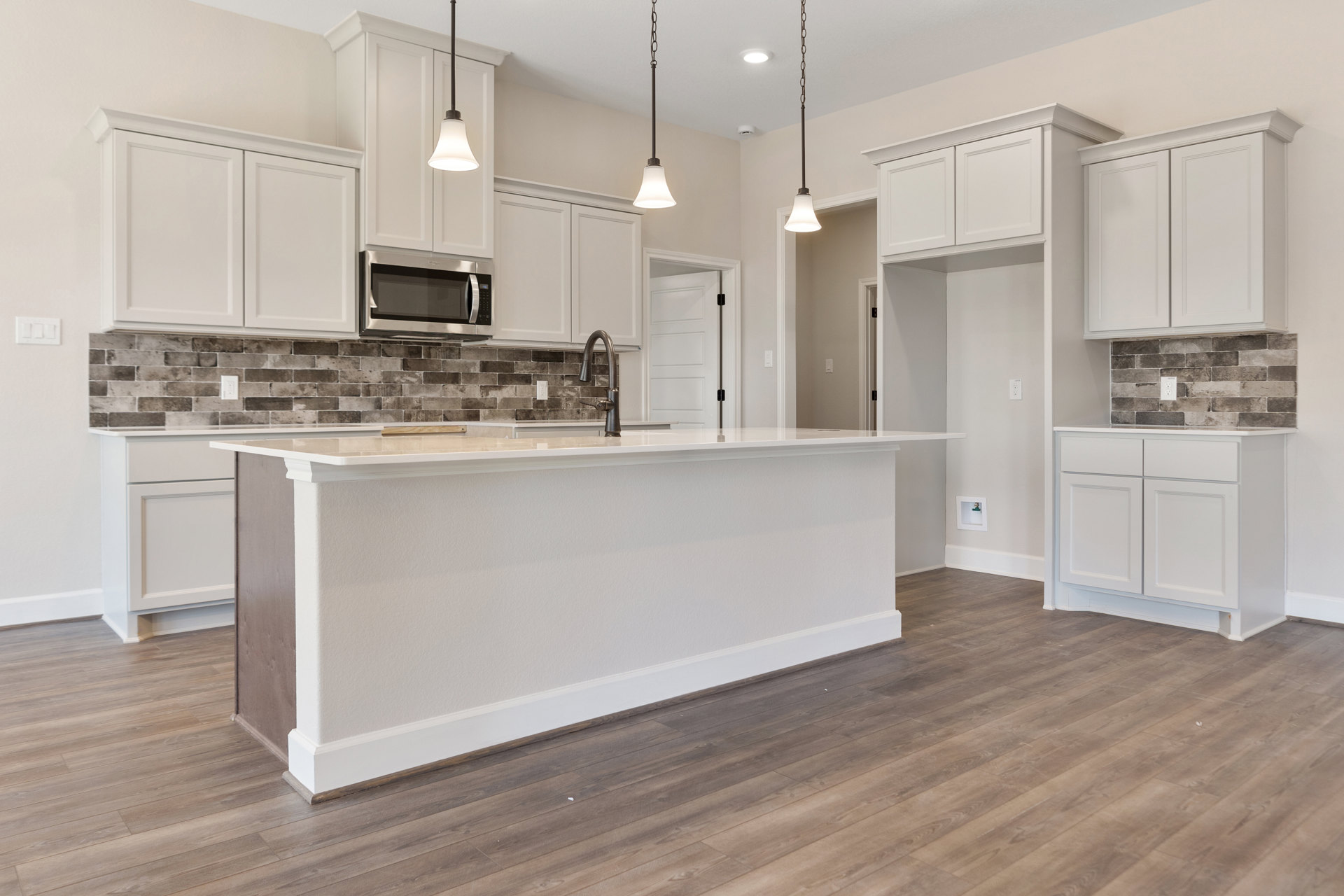 Kitchen with wood flooring, white cabinetry, granite countertops, open microwave door, black lamp on white counter, metal pole detail, white-shaded light fixture