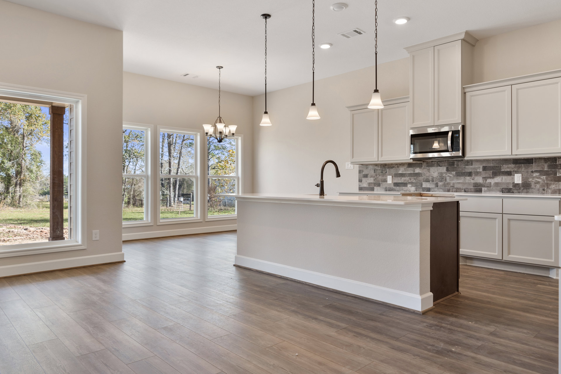 Open-concept kitchen and living room featuring wood flooring, white walls, large windows, white countertops with a vase, built-in microwave with illuminated interior, modern